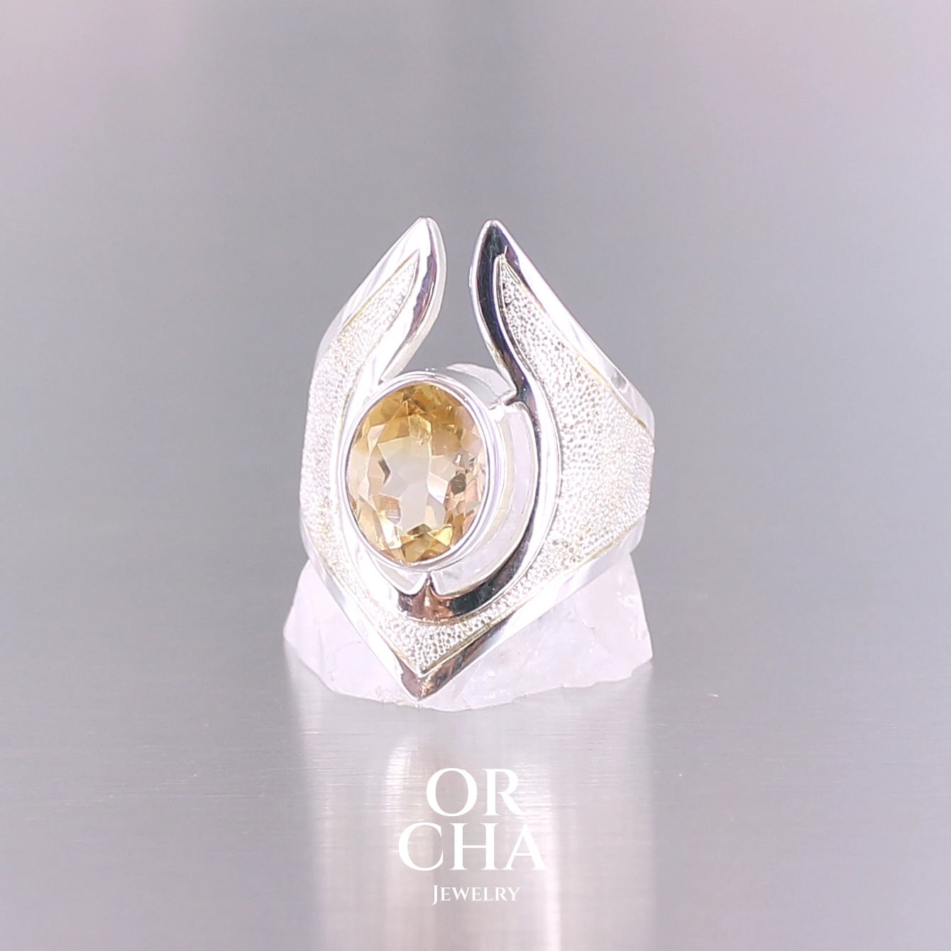 Grande bague contemporaine pour femme en argent massif sertie d'une Citrine. Pierre facettée de forme ovale de qualité transparente, propre à l'oeil. Pierre naturelle de couleur jaune doré lumineux. Bijoux unique, éthique et durable présenté dans un coffret de notre marque, prêt à offrir. Livraison offerte, certificat d'authenticité, service client.
