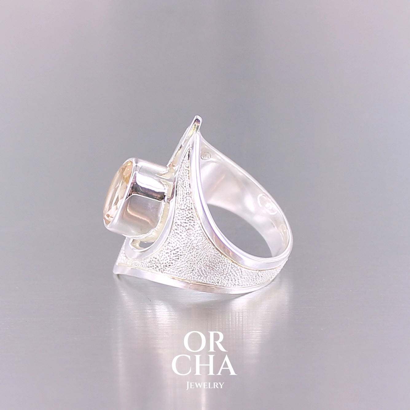 Grande bague contemporaine pour femme en argent massif sertie d'une Citrine. Pierre facettée de forme ovale de qualité transparente, propre à l'oeil. Pierre naturelle de couleur jaune doré lumineux. Bijoux unique, éthique et durable présenté dans un coffret de notre marque, prêt à offrir. Livraison offerte, certificat d'authenticité, service client.
