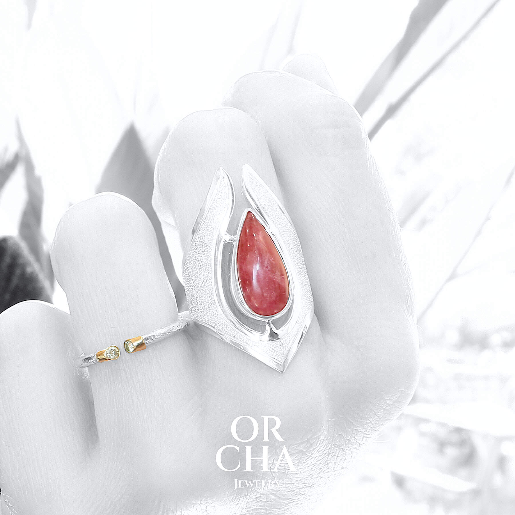 Grande bague porté sur un mannequin pour femme en argent massif sertie d'une Rhodonite. Pierre cabochon en forme de goutte, pierre naturelle de couleur rouge coquelicot. Pierre fine de qualité  opaque à translucide présentant des inclusions. Taille 59. Bijoux unique, éthique et durable présenté dans un coffret de notre marque, prêt à offrir. Livraison offerte, certificat d'authenticité, service client.