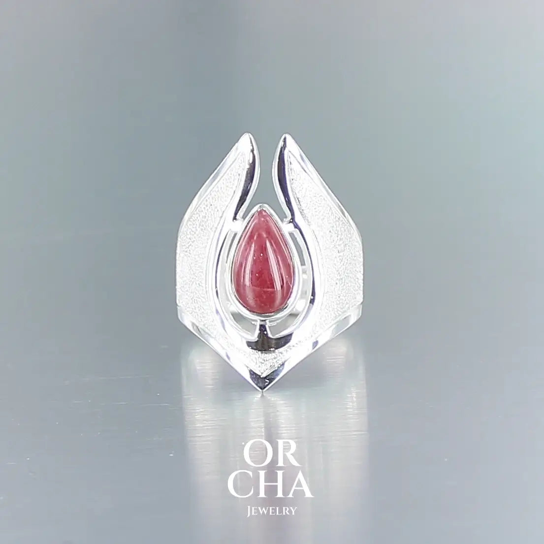 Longue bague pour femme en argent massif sertie d'une Rhodonite. Pierre cabochon en forme de goutte, pierre naturelle de couleur rouge coquelicot. Pierre fine de qualité  opaque à translucide présentant des inclusions. Taille 54. Bijoux unique, éthique et durable présenté dans un coffret de notre marque, prêt à offrir. Livraison offerte, certificat d'authenticité, service client.