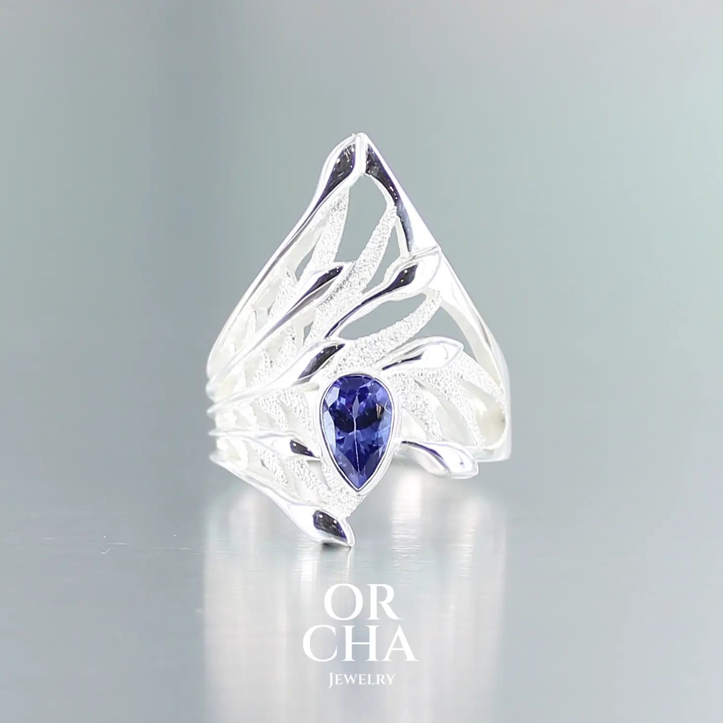 Grande Bague florale pour femme en argent massif sertie d'une Tanzanite. Pierre facettée en forme de goutte, pierre chauffée à la couleur bleue lavande intense. Pierre transparente et propre à l'oeil. Taille 58. Bijoux unique, éthique et durable présenté dans un coffret de notre marque, prêt à offrir. Livraison offerte, certificat d'authenticité, service client.
