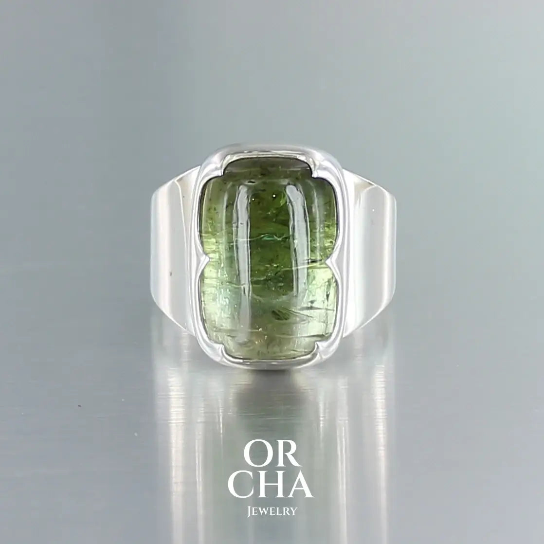 Grande bague pour homme et femme en argent massif sertie d'un cabochon rectangulaire de Tourmaline verte bicolore. Pierre naturelle présentant un camaïeu de vert. Pierre fine de qualité  transparente présentant des inclusions. Taille 58. Bijoux unique, éthique et durable présenté dans un coffret de notre marque, prêt à offrir. Livraison offerte, certificat d'authenticité, service client.
