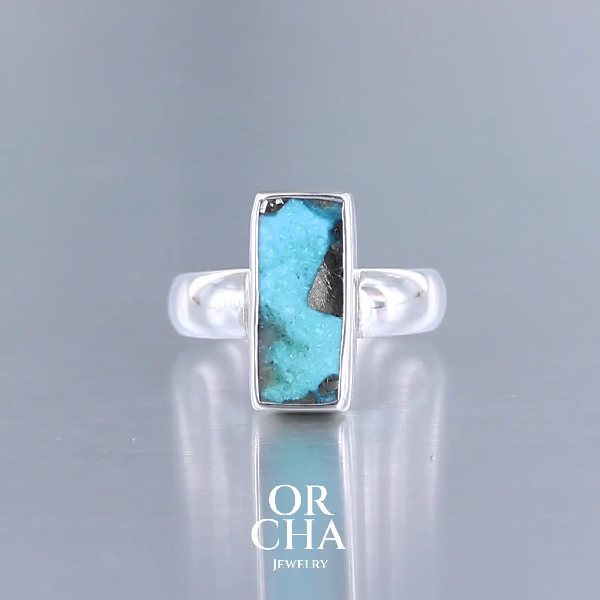 Bague pour femme en argent massif sertie d'une Turquoise perse à inclusions de Pyrite. Tranche polie de turquoise de forme rectangulaire. Pierre de couleur bleu ciel intense à inclusions dorées de pyrite. Qualité opaque. Comme l'immense majorité des Turquoises cette pierre a été stabilisée par traitement. Taille 56. Bijoux unique, éthique et durable présenté dans un coffret de notre marque, prêt à offrir. Livraison offerte, certificat d'authenticité, service client.
