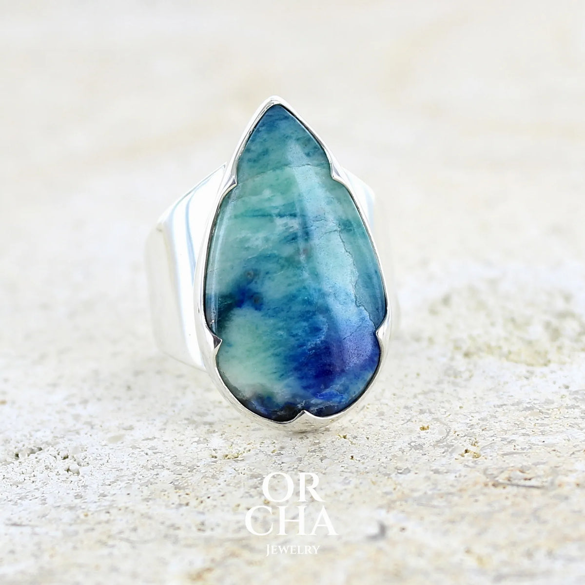 Bague pour femme en argent massif sertie d'un cabochon d'afghane de couleur bleu et bleu gris vert. Pierre taillée en forme de goutte de qualité opaque à inclusions (petites fissures) en surface, fréquentes et admises sur ce type de pierre. Bijou unique réalisée en taille 58 par Orchajewelry