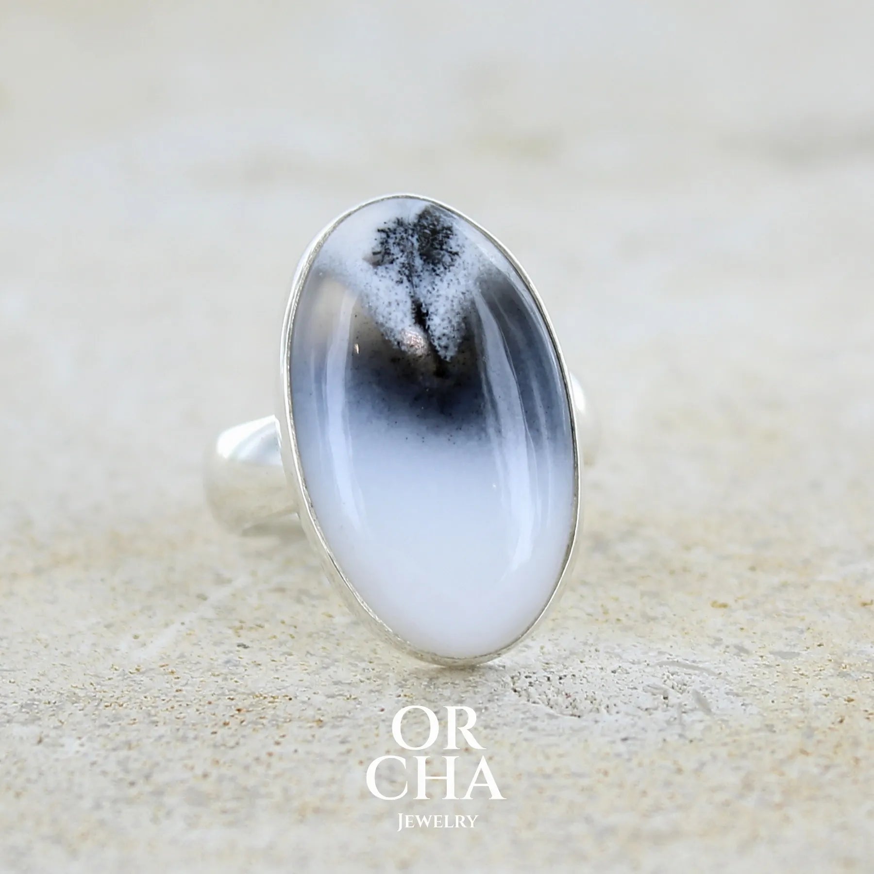Bague pour femme en argent massif sertie d'un cabochon ovale d'agate dendritique de couleur blanc pur et noir. Pierre opaque translucide à inclusions paysages de dendrites de manganèse noires contrastées. Bijou unique réalisée en taille 54 par Orchajewelry