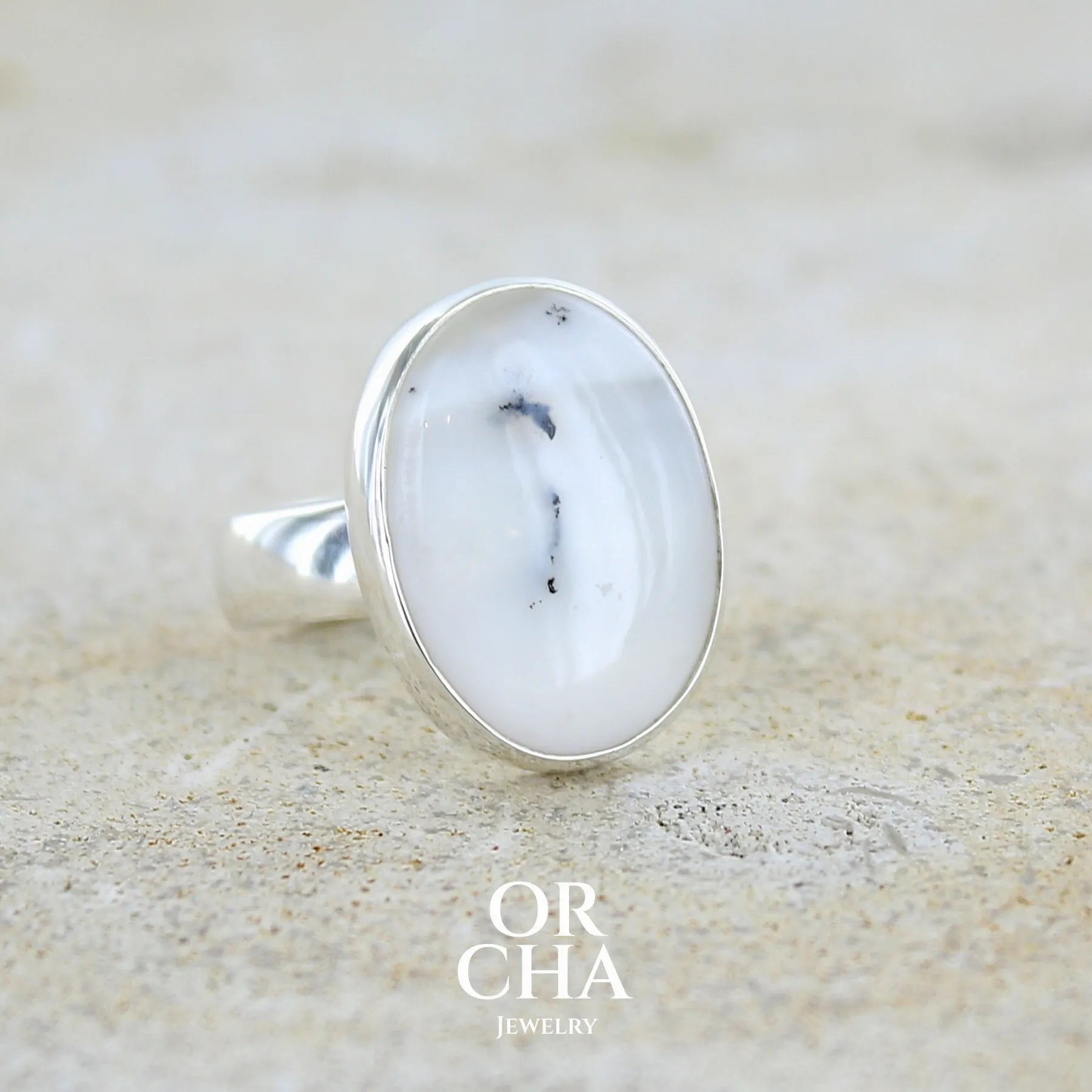 Bague pour femme en argent massif sertie d'un cabochon ovale d'agate dendritique de couleur blanc pur et noir. Pierre opaque à inclusions paysages de dendrites de manganèse noires contrastées. Bijou unique réalisée en taille 54 par Orchajewelry