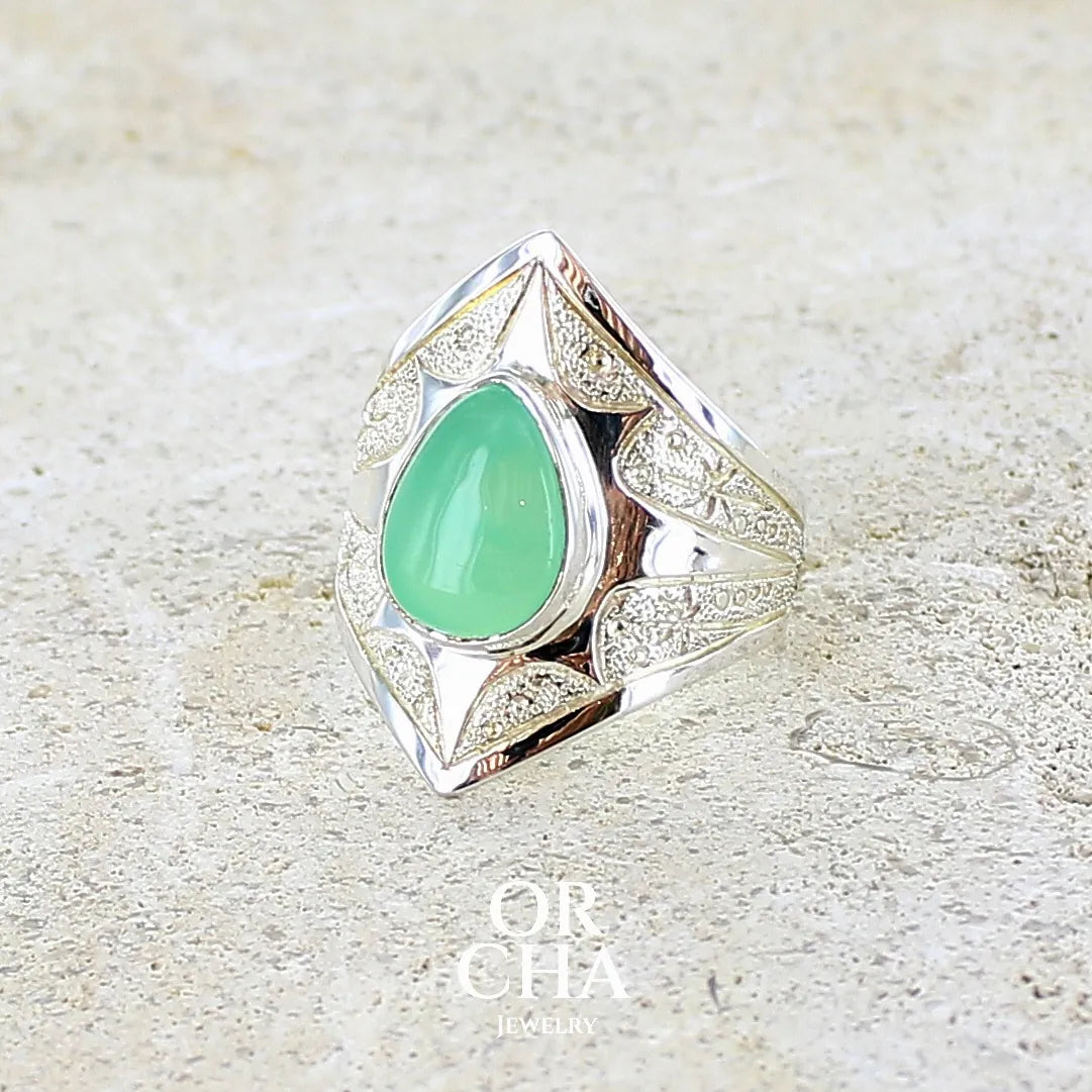 Bague étoile pour femme en argent massif sculptées d'étoiles et autres corps célestes sertie d'un cabochon de chrysoprase de couleur verte pastel. Pierre naturelle de qualité translucide taillée goutte. Bague unique réalisée en taille 57 par Orcha jewelry