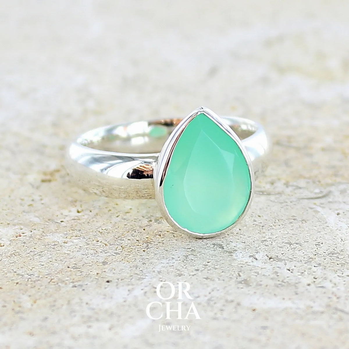 Bague pour femme en argent massif sertie d'un cabochon de chrysoprase de couleur vert émeraude pastel. Pierre translucide taillée en forme de goutte. Bijou unique réalisé en taille 58 par Orcha Jewelry