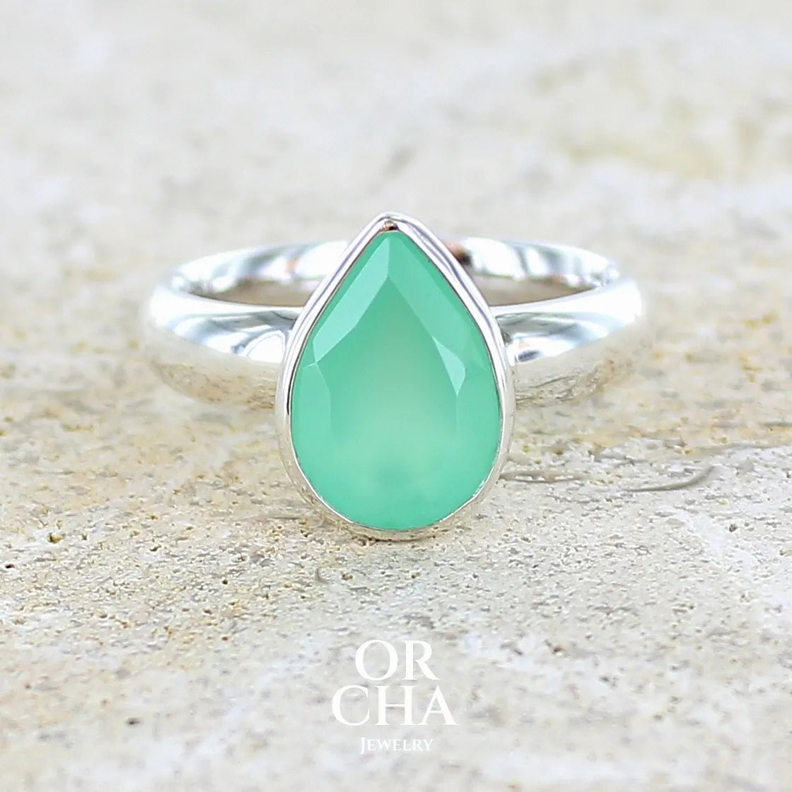 Bague pour femme en argent massif sertie d'un cabochon de chrysoprase de couleur vert émeraude pastel. Pierre translucide taillée en forme de goutte. Bijou unique réalisé en taille 56 par Orcha Jewelry
