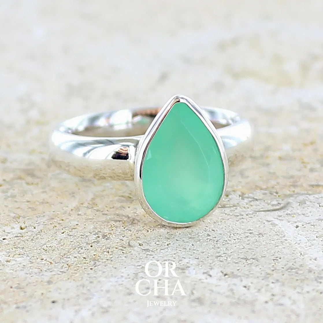 Bague pour femme en argent massif sertie d'un cabochon de chrysoprase de couleur vert émeraude pastel. Pierre translucide taillée en forme de goutte. Bijou unique réalisé en taille 56 par Orcha Jewelry