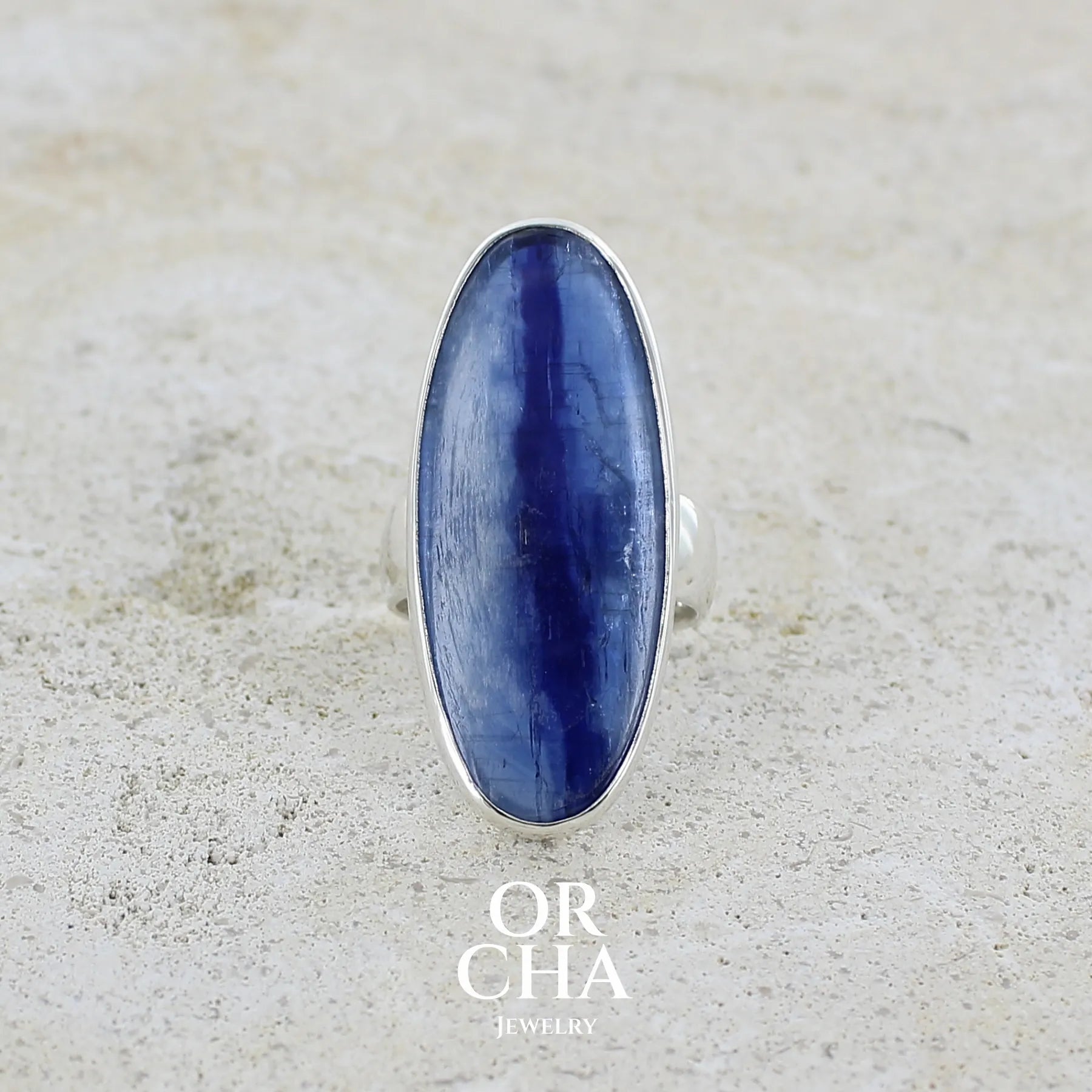 Grande Bague pour femme en argent massif, sertie d'un long cabochon ovale de cyanite de couleur bleu denim nacré. Pierre de qualité translucide. Bijou unique réalisée en taille 58 par Orcha jewelry