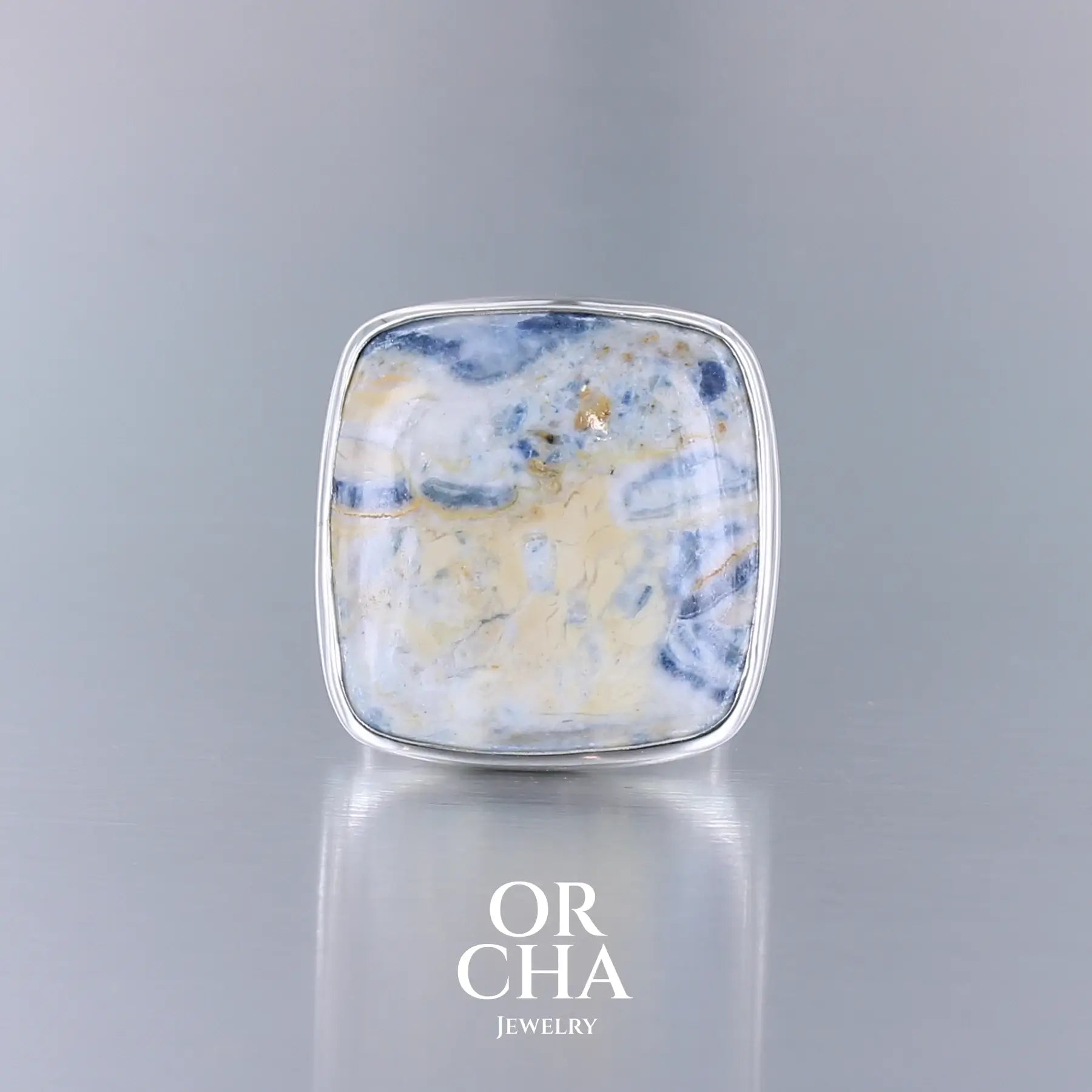 Bague carrée pour femme en argent massif sertie d'une scheelite bleue. Pierre naturelle de couleur bleu, beige creme et blanc de qualité  opaque. Taille 60. Bijoux unique, éthique et durable présenté dans un coffret de notre marque, prêt à offrir. Livraison offerte, certificat d'authenticité, service client.

