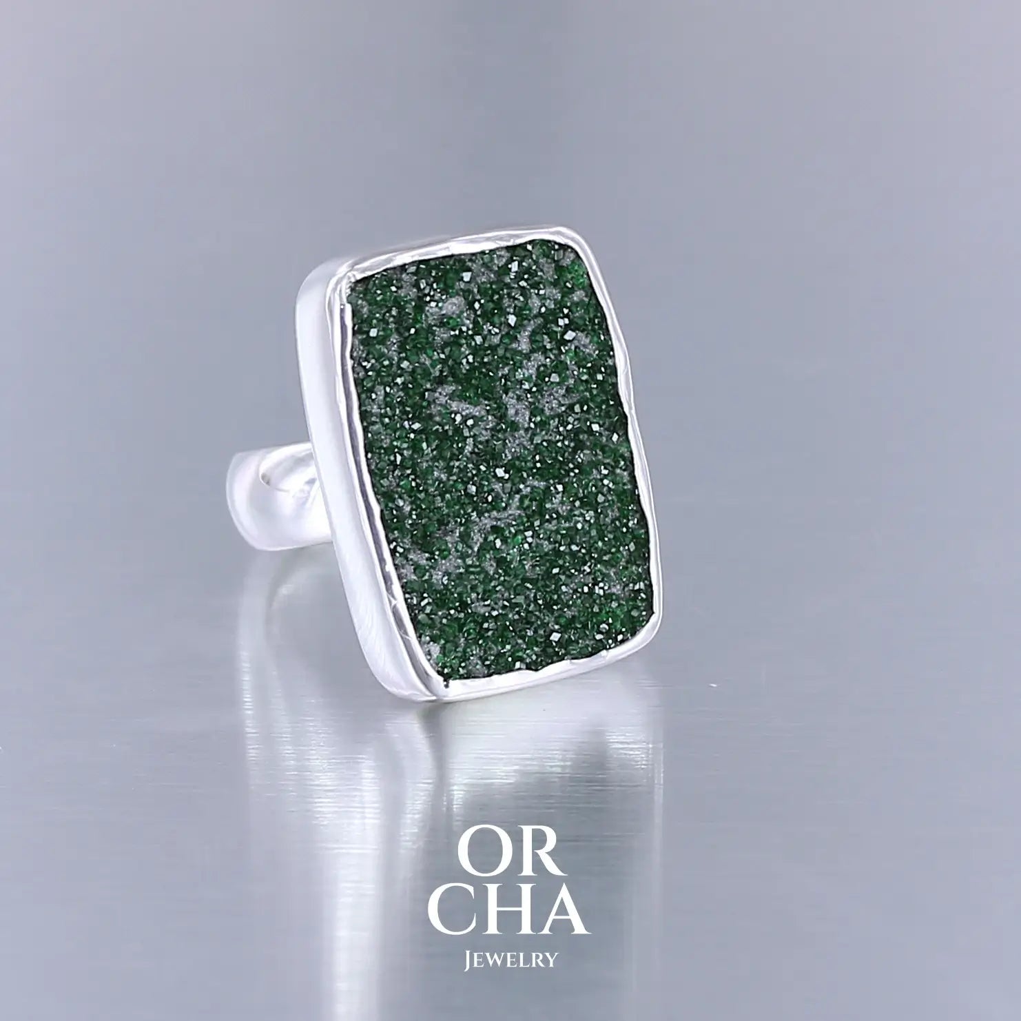 Bague en argent massif sertie d'un grenat Uvarovite brute. Pierre naturelle recouverte de cristaux scintillants de couleur verte. Bague réalisée en taille 55. Bijoux unique, éthique et durable présenté dans un coffret de notre marque, prêt à offrir. Livraison offerte, certificat d'authenticité, service client.