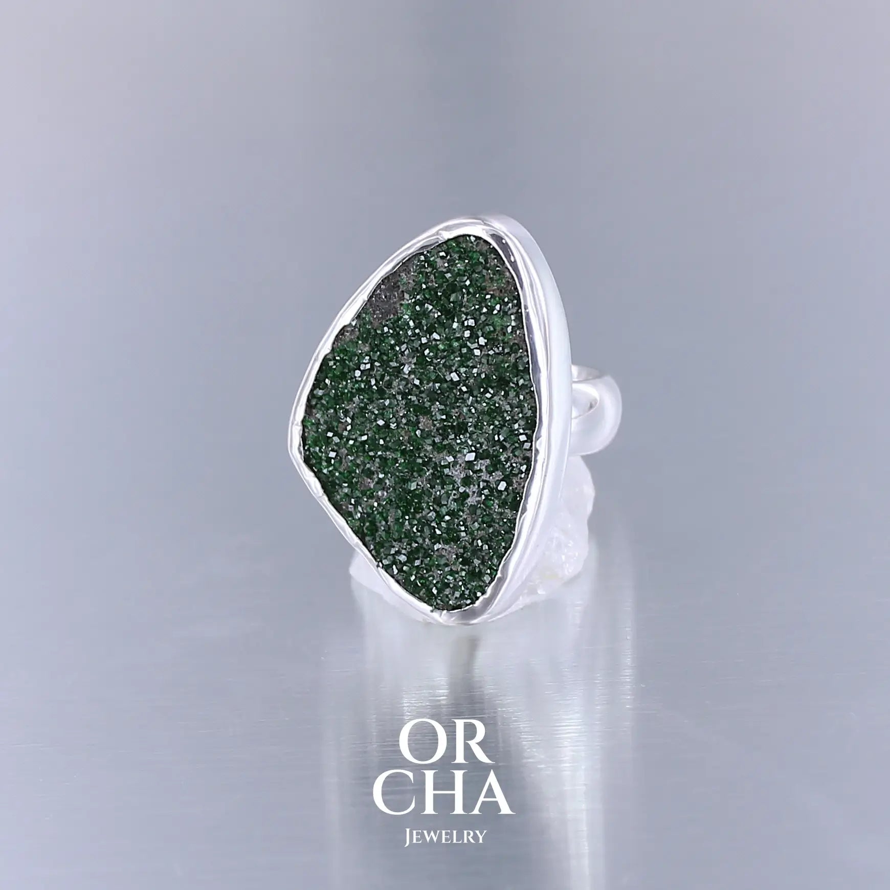 Bague en argent massif serti d'un grenat Uvarovite brute. Pierre naturelle recouverte de cristaux scintillants de couleur verte. Bague réalisée en taille 55. Bijoux unique, éthique et durable présenté dans un coffret de notre marque, prêt à offrir. Livraison offerte, certificat d'authenticité, service client.
