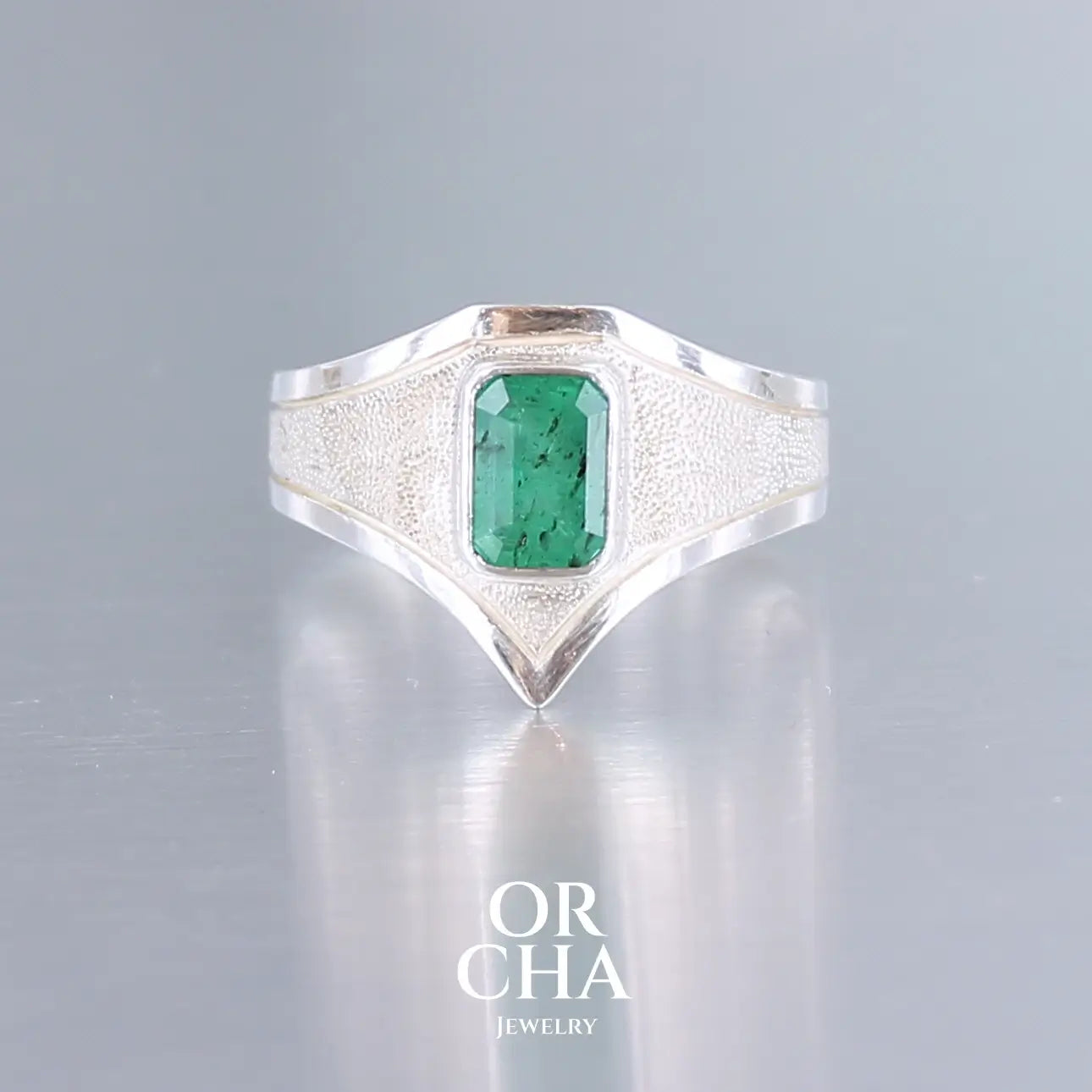 Bague en argent massif sertie d'une émeraude verte taille émeraude, montée en serti clos sur un anneau texturé à forme pointue élégante. Bijou artisanal unique alliant éclat naturel de la pierre et finesse du design contemporain. Bijoux unique, éthique et durable présenté dans un coffret de notre marque, prêt à offrir. Livraison offerte, certificat d'authenticité, service client.