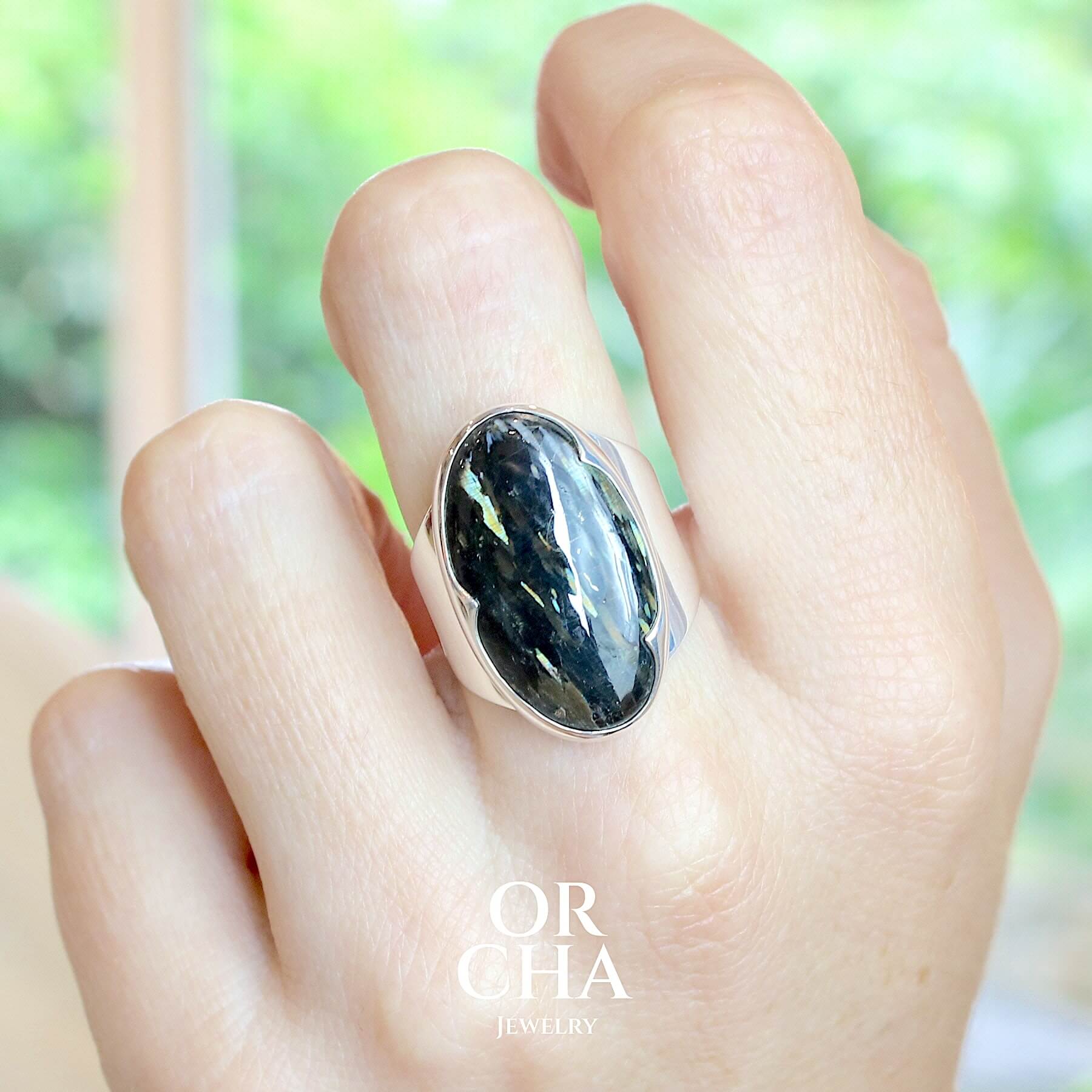 Bague pour femme en argent massif sertie d'une Nuumite. Pierre rare originaire du Groenland, de couleur noir profond cette pierre présente des inclusions lumineuses aux reflets bleus verts dorés. Cabochon de forme ovale. Bague réalisée en taille 56. Bijoux unique, éthique et durable présenté dans un coffret de notre marque, prêt à offrir. Livraison offerte, certificat d'authenticité, service client.