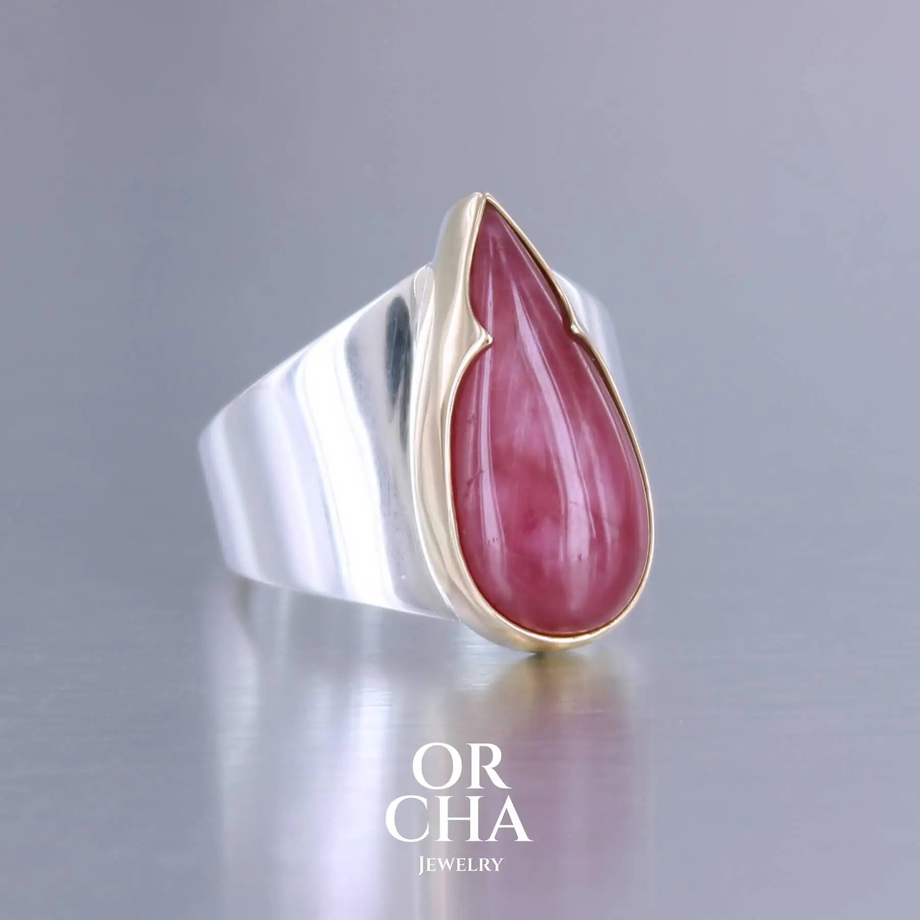 Grande bague pour femme en or 18k et argent massif sertie d'une Rhodonite. Pierre cabochon en forme de goutte, pierre naturelle de qualité rare de couleur rouge coquelicot. Pierre fine de qualité  opaque. Taille 56. Bijoux unique, éthique et durable présenté dans un coffret de notre marque, prêt à offrir. Livraison offerte, certificat d'authenticité, service client.