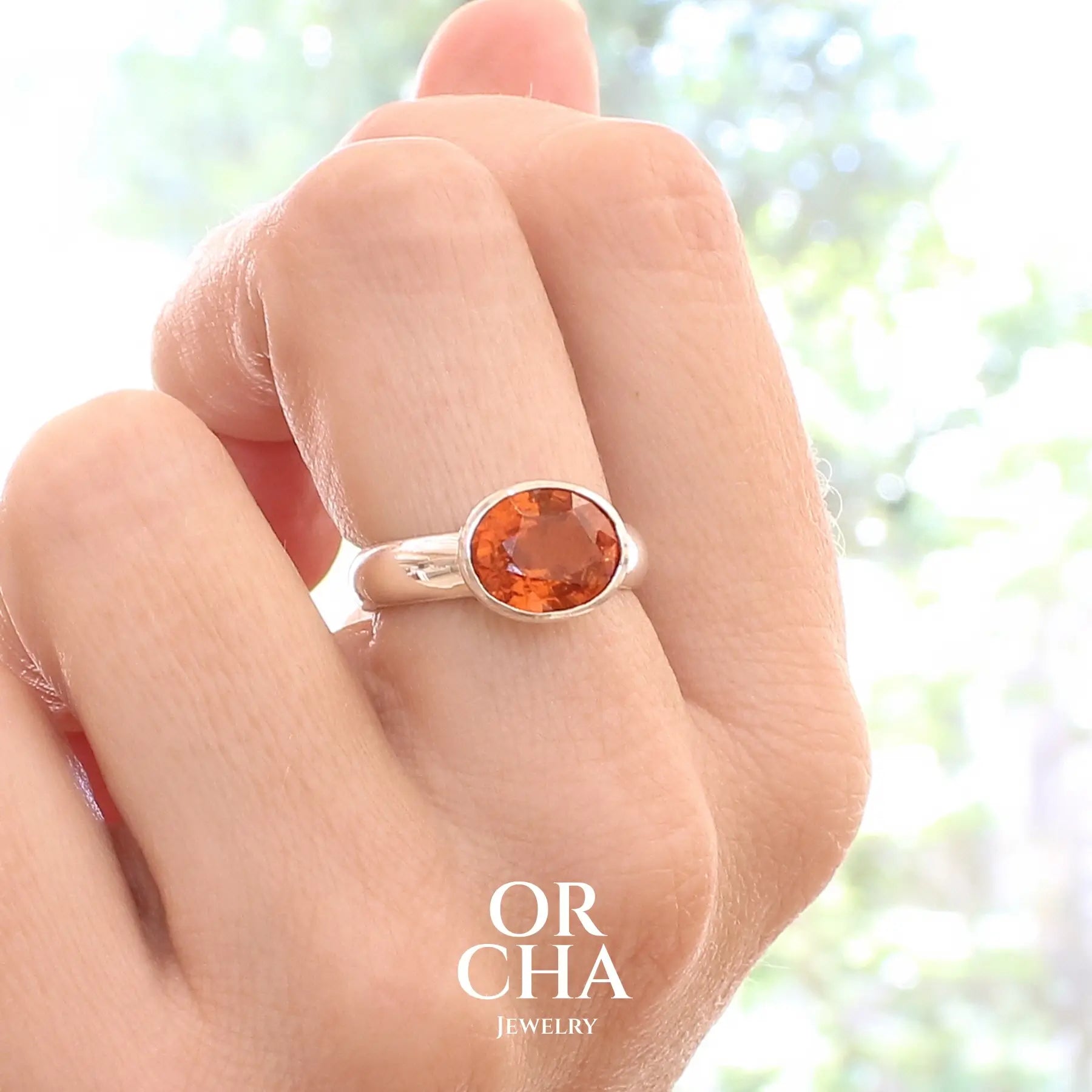 photo sur modèle d'une bague cocktail pour femme en argent massif sertie d'un Grenat Spessartite. Pierre facettée de forme ovale de qualité transparente, propre à l'oeil. Pierre naturelle de couleur orange intense, ce Grenat est également appelé Grenat "Fanta" en rapport à la couleur saturé du célèbre soda. Tailles 58.5.  Bijoux unique, éthique et durable présenté dans un coffret de notre marque, prêt à offrir. Livraison offerte, certificat d'authenticité, service client.