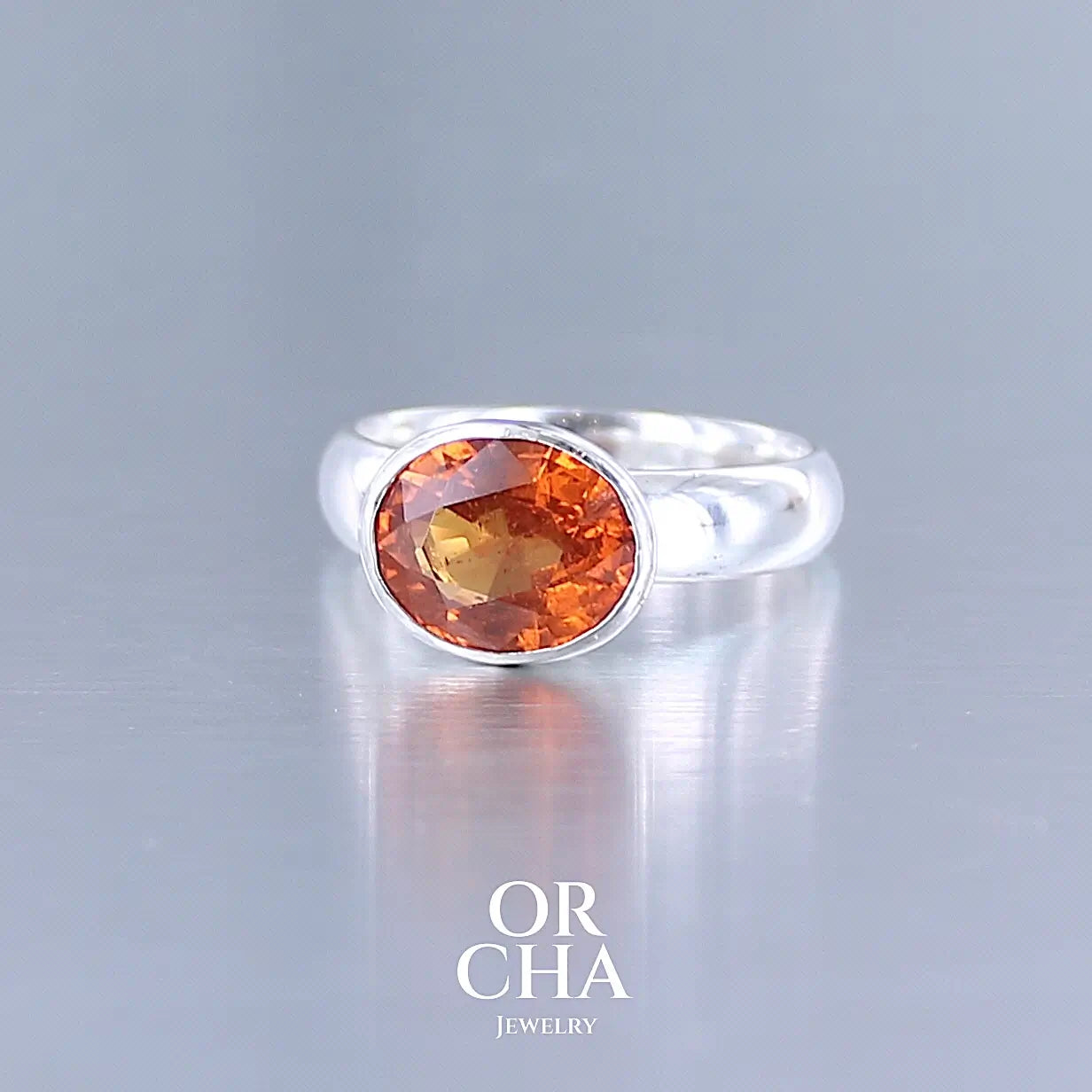 Profil d'une bague cocktail pour femme en argent massif sertie d'un Grenat Spessartite. Pierre facettée de forme ovale de qualité transparente, propre à l'oeil. Pierre naturelle de couleur orange intense, ce Grenat est également appelé Grenat "Fanta" en rapport à la couleur saturé du célèbre soda. Tailles 58.5.  Bijoux unique, éthique et durable présenté dans un coffret de notre marque, prêt à offrir. Livraison offerte, certificat d'authenticité, service client.