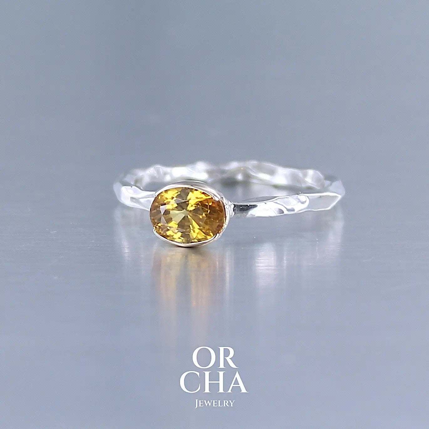 Photo de profil d'une bague anneau pour femme en argent massif et or 12 k sertie d'un Saphir jaune orangé très lumineux. Pierre facettée de forme ovale, de qualité transparente, propre à l'oeil. Pierre chauffée et traitée au beryllium. Bijoux unique, éthique et durable présenté dans un coffret de notre marque, prêt à offrir. Livraison offerte, certificat d'authenticité, service client.