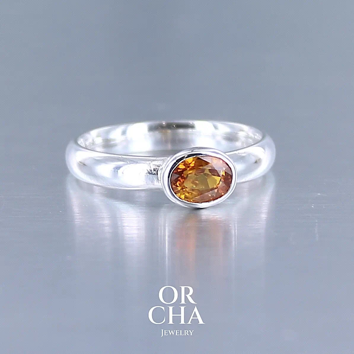 photo de profil d'une bague anneau en argent massif sertie d'un Saphir orange. Pierre facettée de forme ovale de qualité transparente, propre à l'oeil. Pierre chauffe et traité au beryllium de couleur orange intense. Tailles 56. Pour homme et femme. Bijoux unique, éthique et durable présenté dans un coffret de notre marque, prêt à offrir. Livraison offerte, certificat d'authenticité, service client.