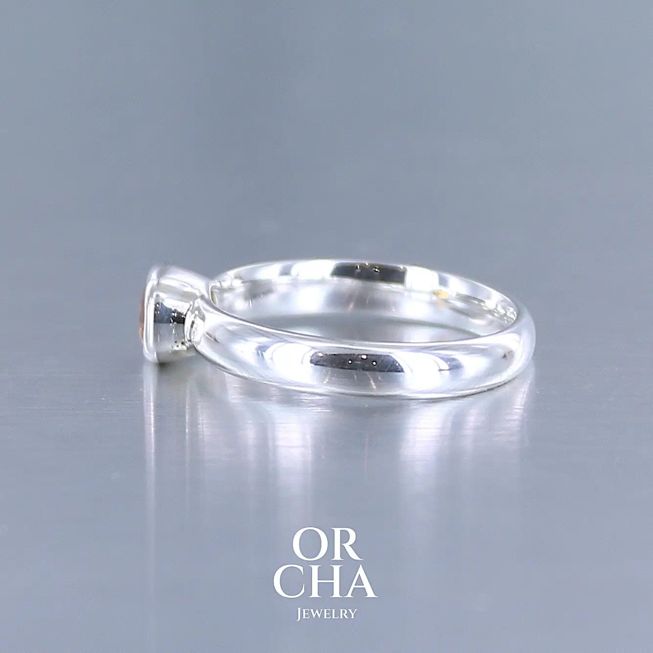 photo de profil d'une bague anneau en argent massif sertie d'un Saphir orange. Pierre facettée de forme ovale de qualité transparente, propre à l'oeil. Pierre chauffe et traité au beryllium de couleur orange intense. Tailles 56. Pour homme et femme. Bijoux unique, éthique et durable présenté dans un coffret de notre marque, prêt à offrir. Livraison offerte, certificat d'authenticité, service client.