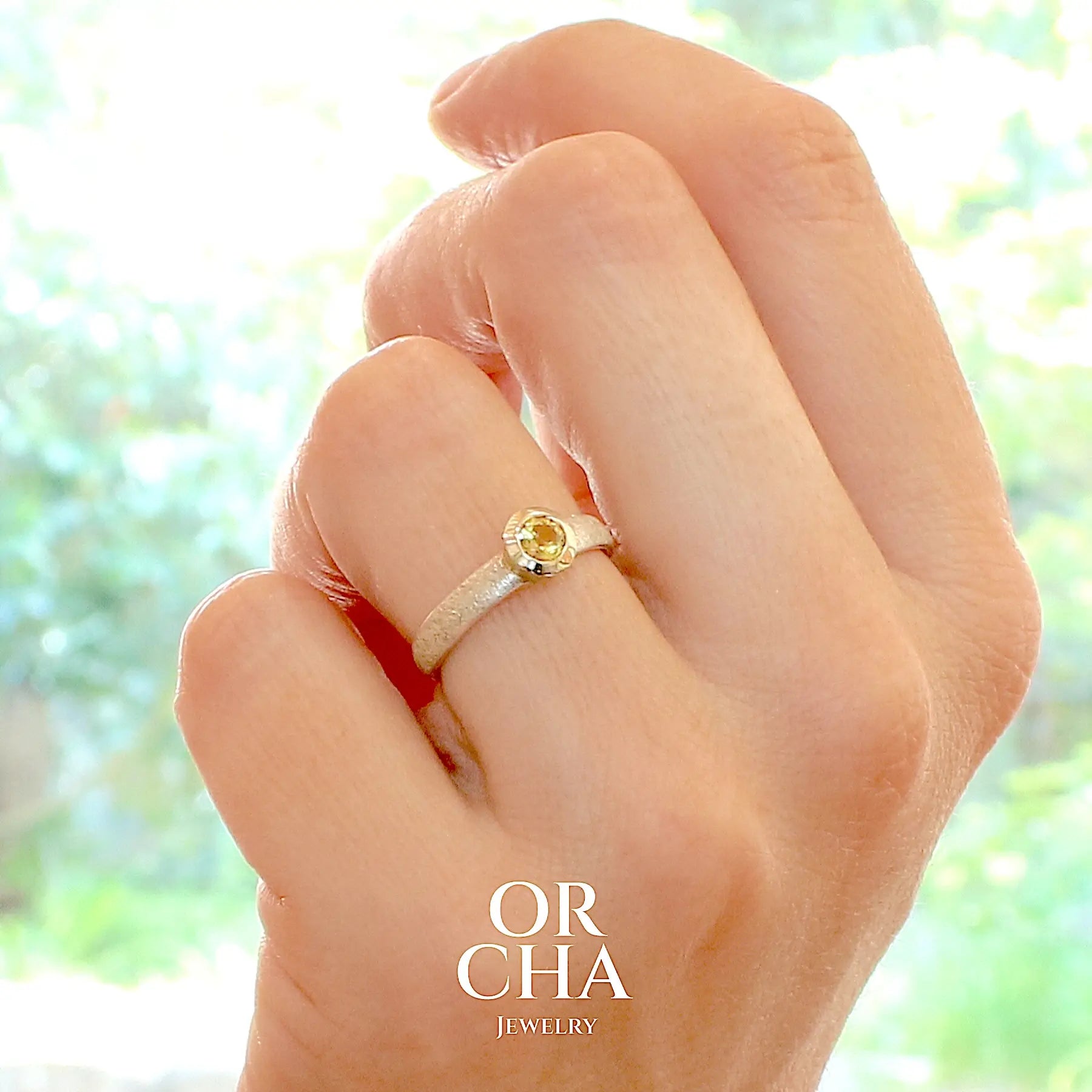 Photo d'une main qui porte une Bague anneau pour femme en argent massif et or sertie d'une Héliodore. Pierre facettée de forme ronde, de qualité transparente, propre à l'oeil. Pierre naturelle de couleur jaune doré lumineux. Bijoux unique, éthique et durable présenté dans un coffret de notre marque, prêt à offrir. Livraison offerte, certificat d'authenticité, service client.
