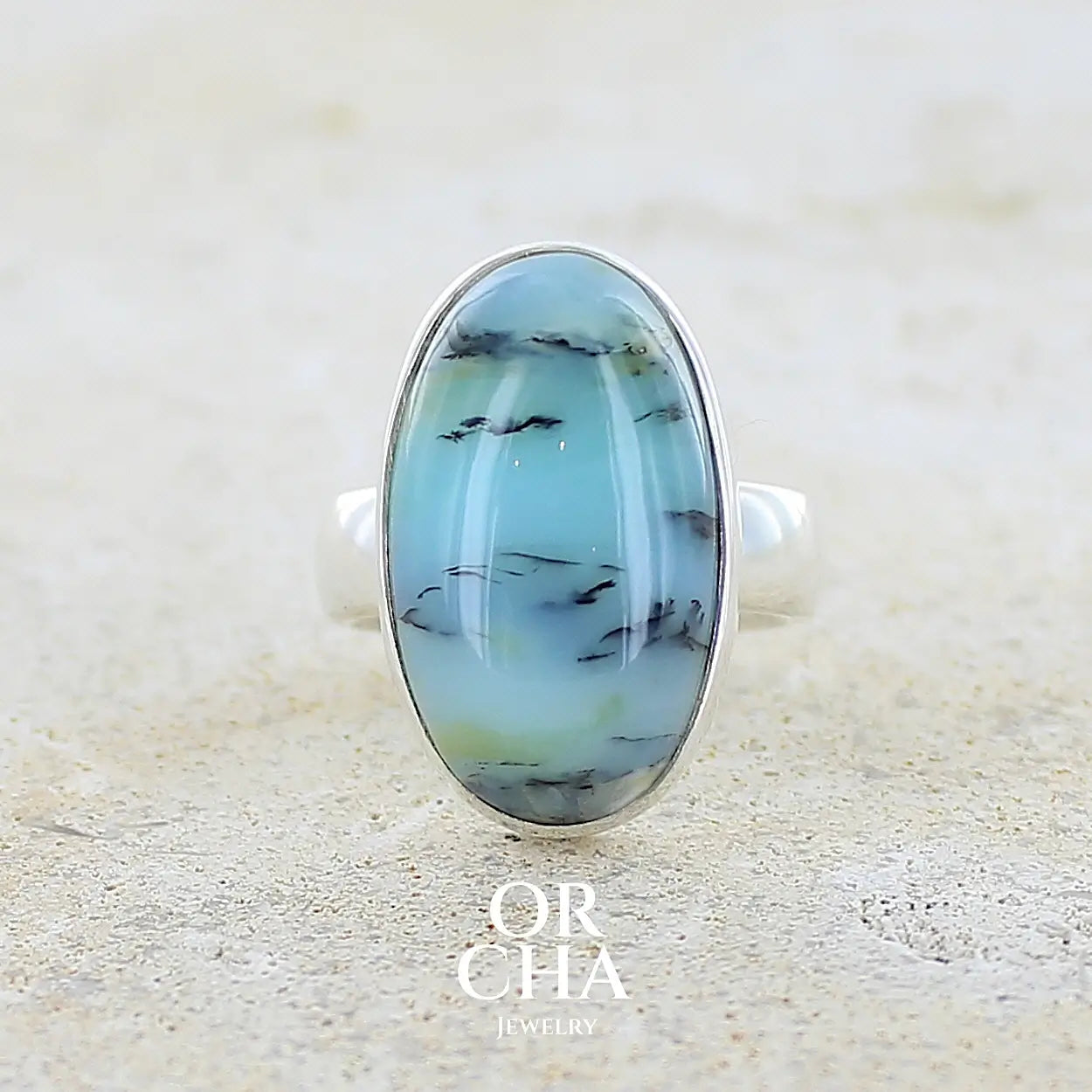 Bague pour femme en argent massif, sertie d'un cabochon ovale d'opale bleue du Pérou de couleur bleu laiteux à inclusions de dendrites noires. Pierre naturelle de qualité opaque et translucide. Bijoux unique réalisé en taille 54,5 - OrchaJewelry