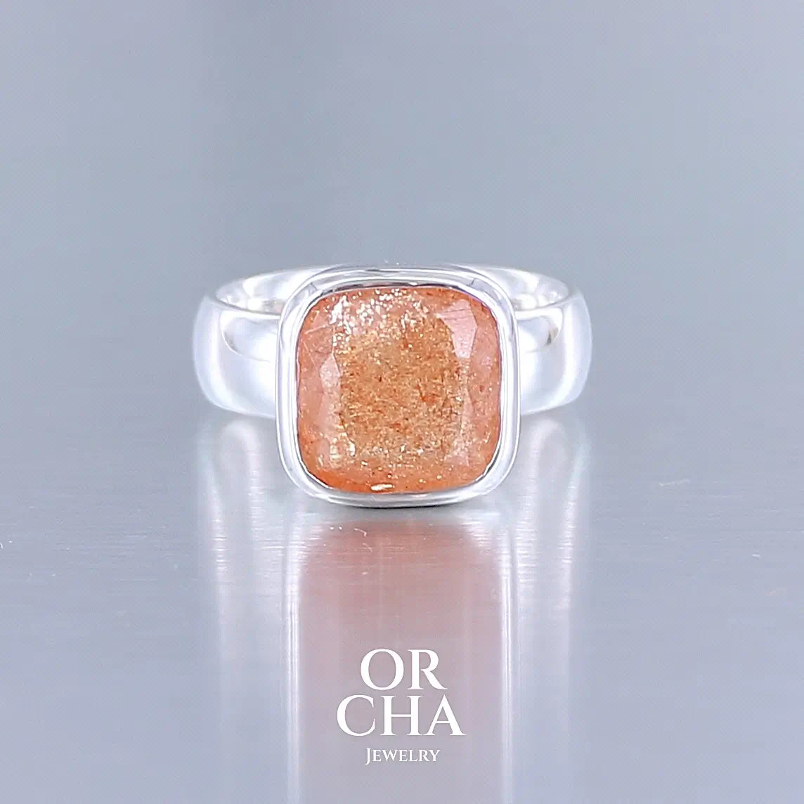 Bague cocktail pour femme en argent massif sertie d'une pierre de soleil oranges de très belle qualité, pierre transparente avec inclusions scintillantes d'hématites. Pierre naturelle facettée de forme carrée. Tailles 56. Bijoux unique, éthique et durable présenté dans un coffret de notre marque, prêt à offrir. Livraison offerte, certificat d'authenticité, service client.