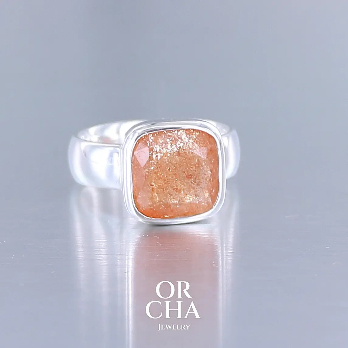 photo de profil d'une bague cocktail pour femme en argent massif sertie d'une pierre de soleil oranges de très belle qualité, pierre transparente avec inclusions scintillantes d'hématites. Pierre naturelle facettée de forme carrée. Tailles 56. Bijoux unique, éthique et durable présenté dans un coffret de notre marque, prêt à offrir. Livraison offerte, certificat d'authenticité, service client.