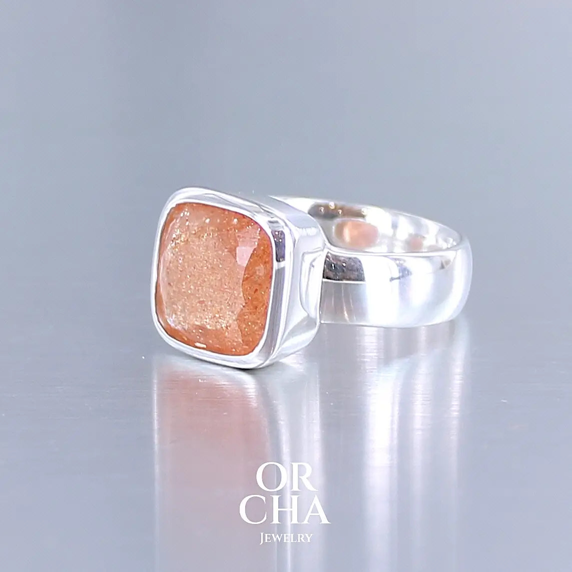 photo de profil d'une bague cocktail pour femme en argent massif sertie d'une pierre de soleil oranges de très belle qualité, pierre transparente avec inclusions scintillantes d'hématites. Pierre naturelle facettée de forme carrée. Tailles 56. Bijoux unique, éthique et durable présenté dans un coffret de notre marque, prêt à offrir. Livraison offerte, certificat d'authenticité, service client.