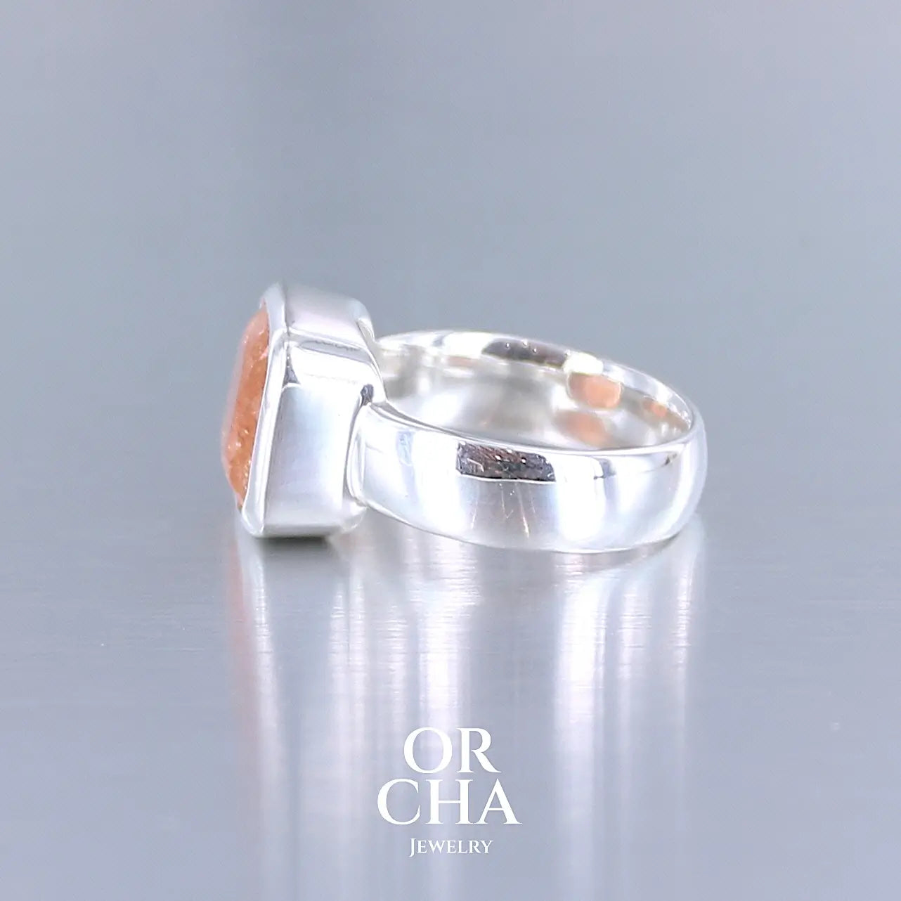 photo de profil d'une bague cocktail pour femme en argent massif sertie d'une pierre de soleil oranges de très belle qualité, pierre transparente avec inclusions scintillantes d'hématites. Pierre naturelle facettée de forme carrée. Tailles 56. Bijoux unique, éthique et durable présenté dans un coffret de notre marque, prêt à offrir. Livraison offerte, certificat d'authenticité, service client.