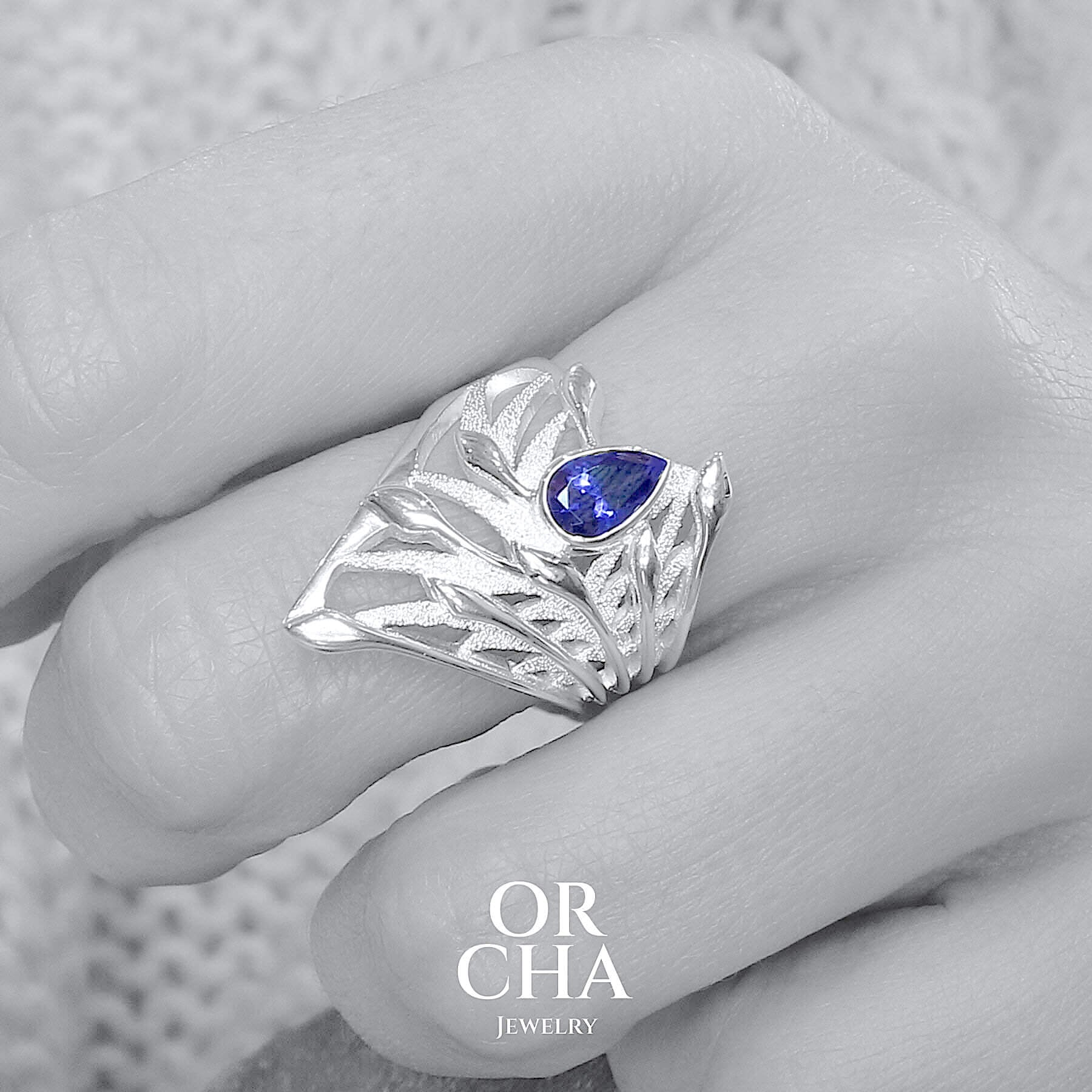 photo portée d'une grande Bague florale pour femme en argent massif sertie d'une Tanzanite. Pierre facettée en forme de goutte, pierre chauffée à la couleur bleue lavande intense. Pierre transparente et propre à l'oeil. Taille 58. Bijoux unique, éthique et durable présenté dans un coffret de notre marque, prêt à offrir. Livraison offerte, certificat d'authenticité, service client.
