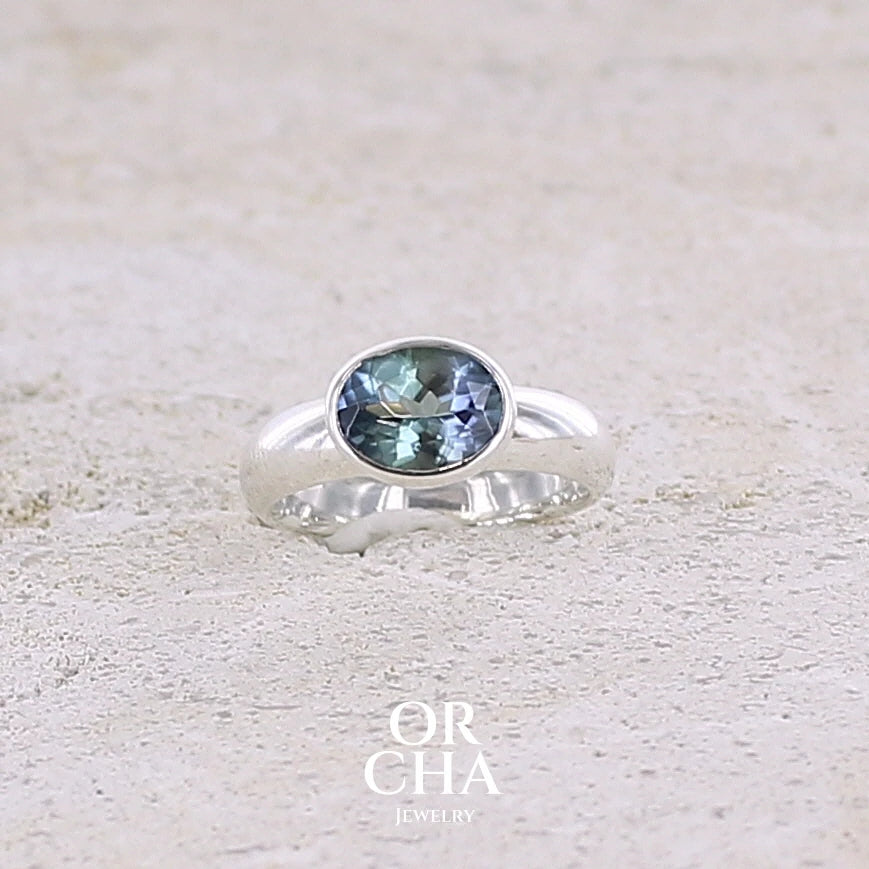 Bague solitaire pour femme en argent massif sertie d'une tanzanite bicolore. Pierre facettée de forme ovale de qualité transparente, propre à l'oeil. Pierre naturelle de couleur bleu verte et logés reflets violets. Bague réalisée en taille 50. Bijoux unique, éthique et durable présenté dans un coffret de notre marque, prêt à offrir. Livraison offerte, certificat d'authenticité, service client.