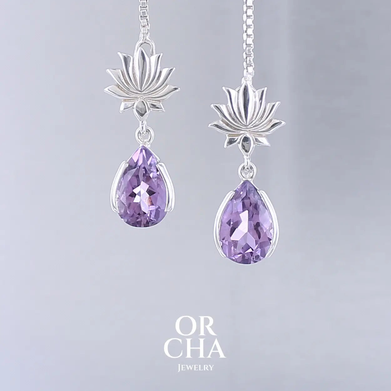 Boucles d'oreilles Lotus pour femme en argent massif serties d'Améthystes. Pierres facettées en forme de gouttes de qualités transparentes, propre à l'oeil. Pierres naturelles de couleurs violettes moyen. Bijoux unique, éthique et durable présenté dans un coffret de notre marque, prêt à offrir. Livraison offerte, certificat d'authenticité, service client.