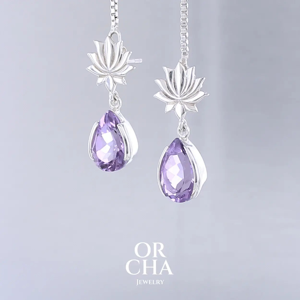 Boucles d'oreilles Lotus pour femme en argent massif serties d'Améthystes. Pierres facettées en forme de gouttes de qualités transparentes, propre à l'oeil. Pierres naturelles de couleurs violettes moyen. Bijoux unique, éthique et durable présenté dans un coffret de notre marque, prêt à offrir. Livraison offerte, certificat d'authenticité, service client.