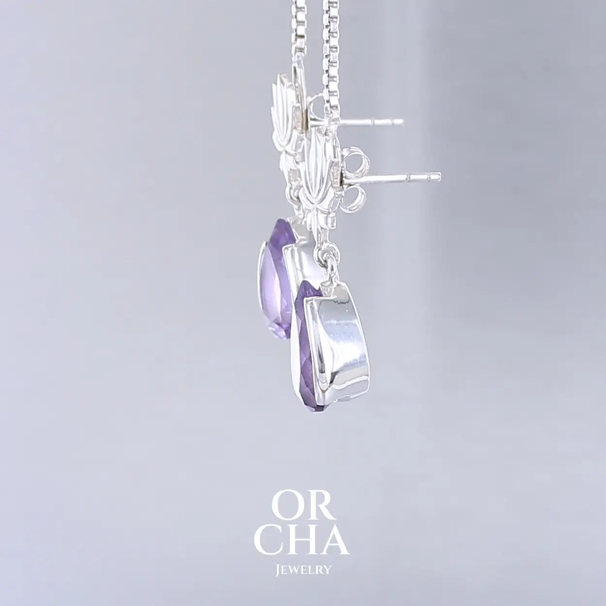 Boucles d'oreilles Lotus pour femme en argent massif serties d'Améthystes. Pierres facettées en forme de gouttes de qualités transparentes, propre à l'oeil. Pierres naturelles de couleurs violettes moyen. Bijoux unique, éthique et durable présenté dans un coffret de notre marque, prêt à offrir. Livraison offerte, certificat d'authenticité, service client.