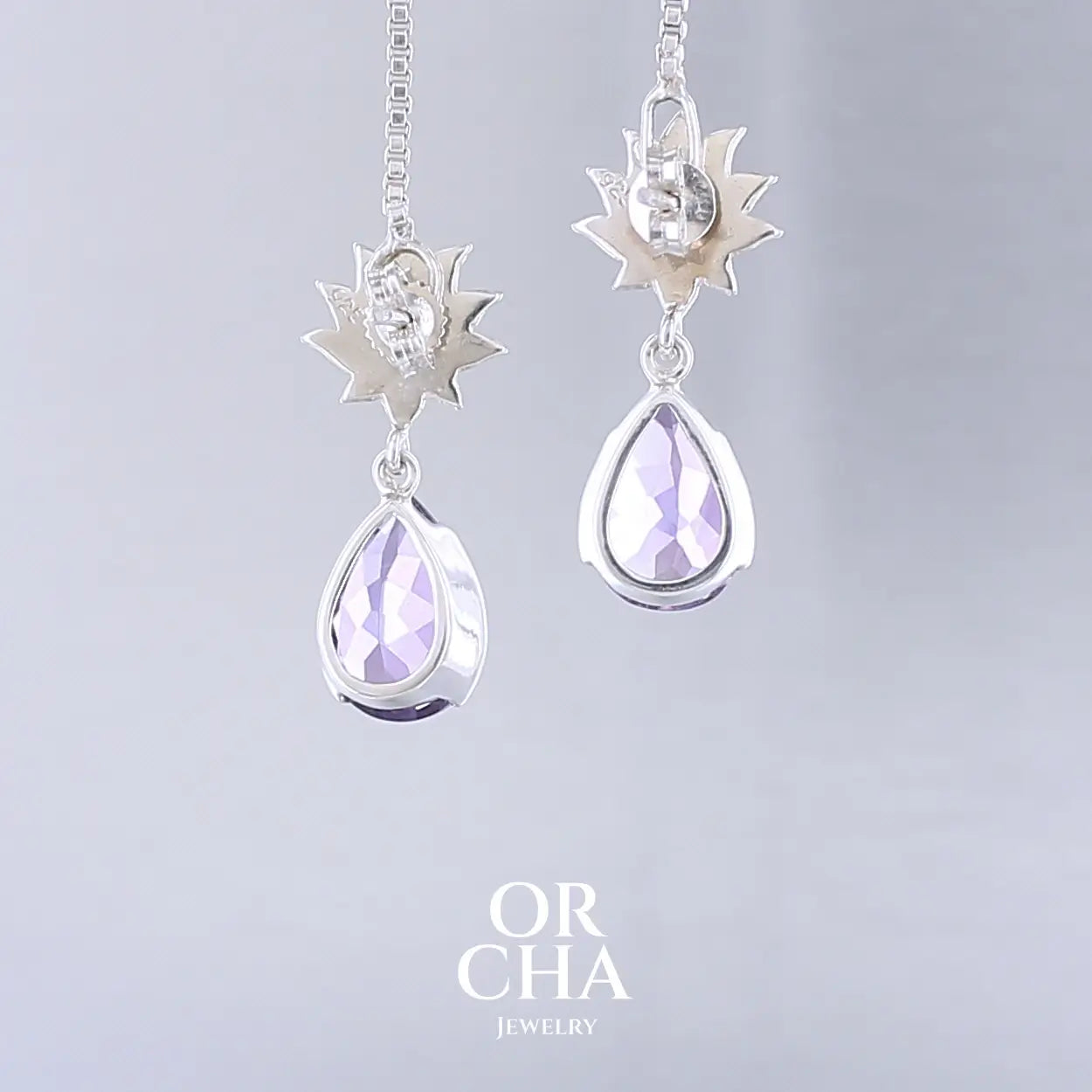 Boucles d'oreilles Lotus pour femme en argent massif serties d'Améthystes. Pierres facettées en forme de gouttes de qualités transparentes, propre à l'oeil. Pierres naturelles de couleurs violettes moyen. Bijoux unique, éthique et durable présenté dans un coffret de notre marque, prêt à offrir. Livraison offerte, certificat d'authenticité, service client.