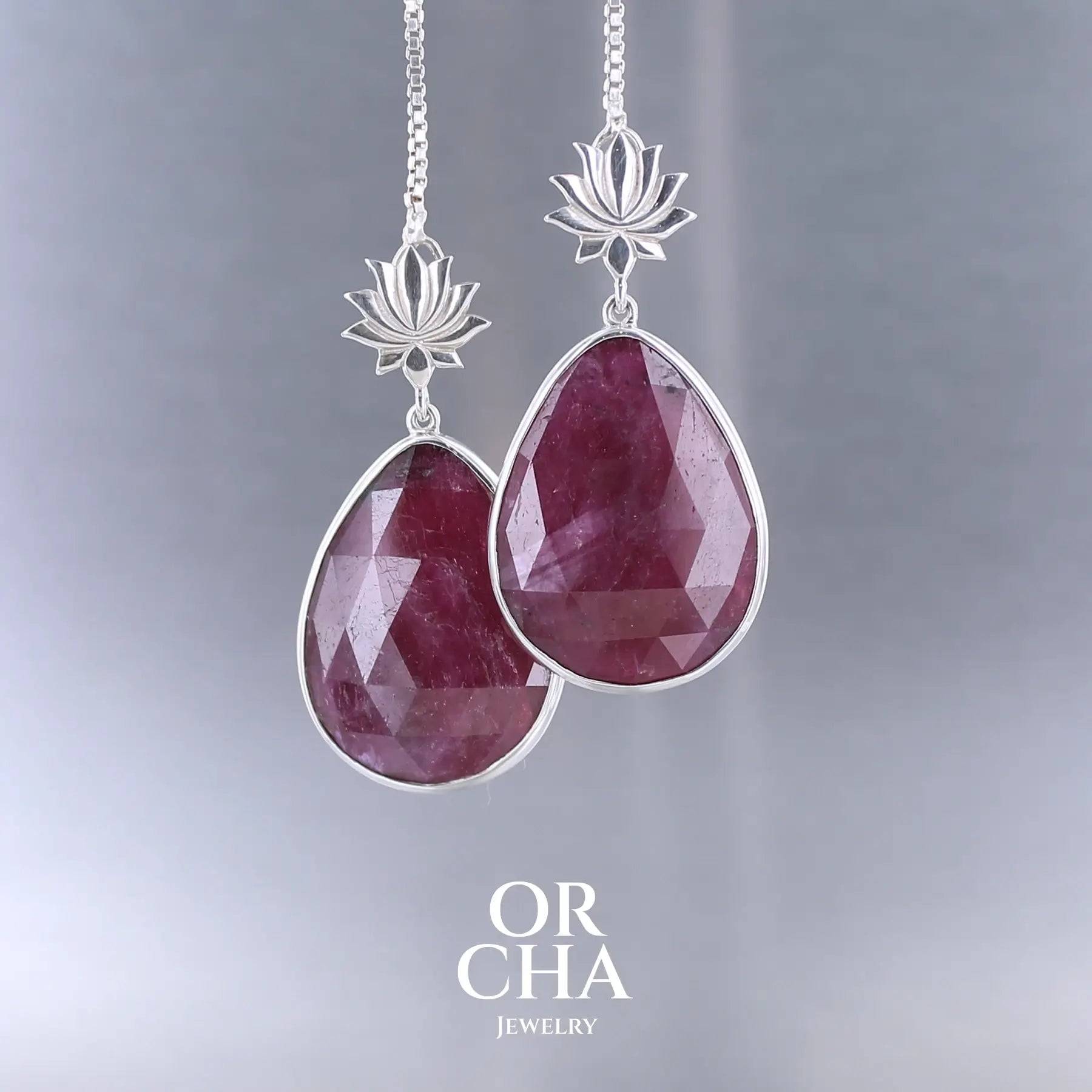 Boucles d'oreilles lotus pour femme en argent massif sertie de rubis. Cabochons facettés en forme de goutte de qualité opaque. Pierre naturelle de couleur rouge violacé. Le clou des boucles représente un lotus. Bijoux unique, éthique et durable présenté dans un coffret de notre marque, prêt à offrir. Livraison offerte, certificat d'authenticité, service client.