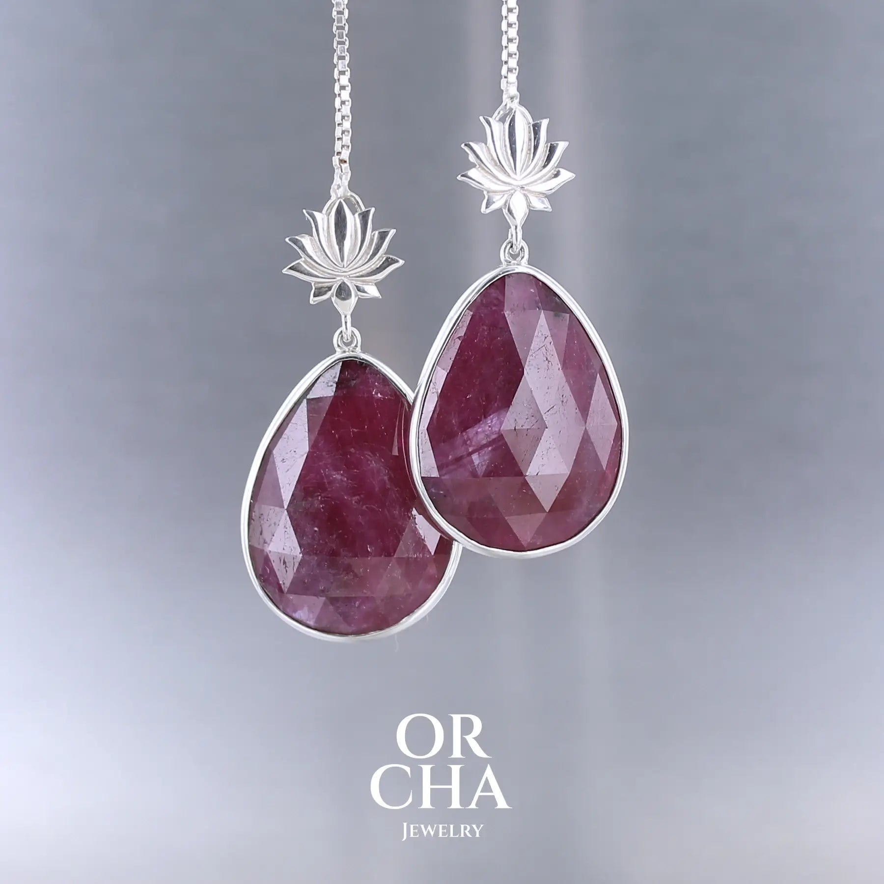 Boucles d'oreilles lotus pour femme en argent massif sertie de rubis. Cabochons facettés en forme de goutte de qualité opaque. Pierre naturelle de couleur rouge violacé. Le clou des boucles représente un lotus. Bijoux unique, éthique et durable présenté dans un coffret de notre marque, prêt à offrir. Livraison offerte, certificat d'authenticité, service client.