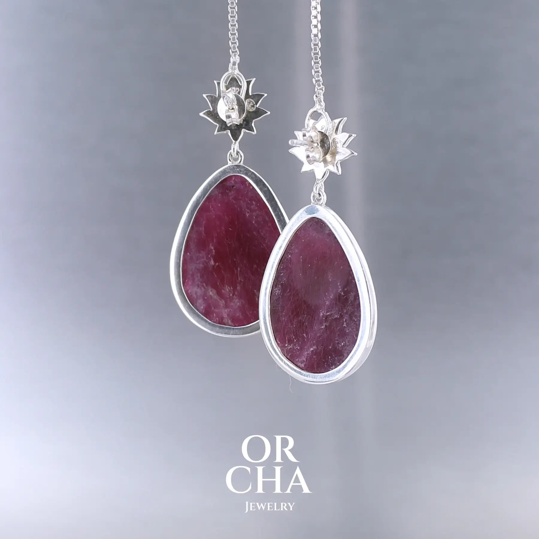 Boucles d'oreilles lotus pour femme en argent massif sertie de rubis. Cabochons facettés en forme de goutte de qualité opaque. Pierre naturelle de couleur rouge violacé. Le clou des boucles représente un lotus. Bijoux unique, éthique et durable présenté dans un coffret de notre marque, prêt à offrir. Livraison offerte, certificat d'authenticité, service client.