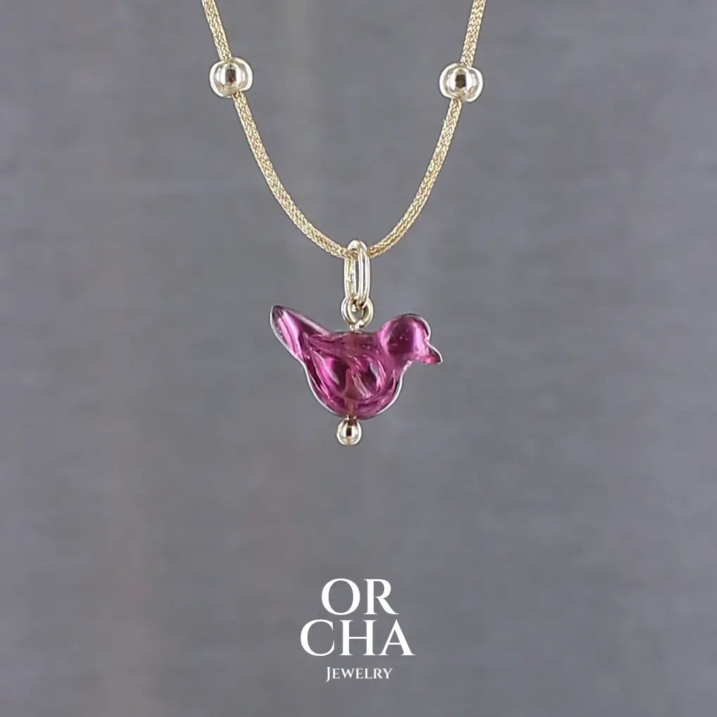 Collier pour femme orné d'une tourmaline rouge violacé sculptée à la main en 3 dimensions en forme d'oiseau sertie en or 18k. Le pendentif est monté sur un collier corde doré scintillant, les apprêts utilisé sont en Gold filled ( or laminé ). Longueur ajustable de 40 cm à 45 cm. Bijoux unique, éthique et durable présenté dans un coffret de notre marque, prêt à offrir. Livraison offerte, certificat d'authenticité, service client.
