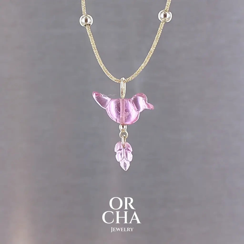 Collier pour femme orné d'une tourmaline rose sculptée à la main en 3 dimensions en forme d'oiseau et de feuille, serties en or 18k. Le pendentif est monté sur un collier corde doré scintillant, les apprêts utilisé sont en Gold filled ( or laminé ). Longueur ajustable de 40 cm à 45 cm. Bijoux unique, éthique et durable présenté dans un coffret de notre marque, prêt à offrir. Livraison offerte, certificat d'authenticité, service client.
