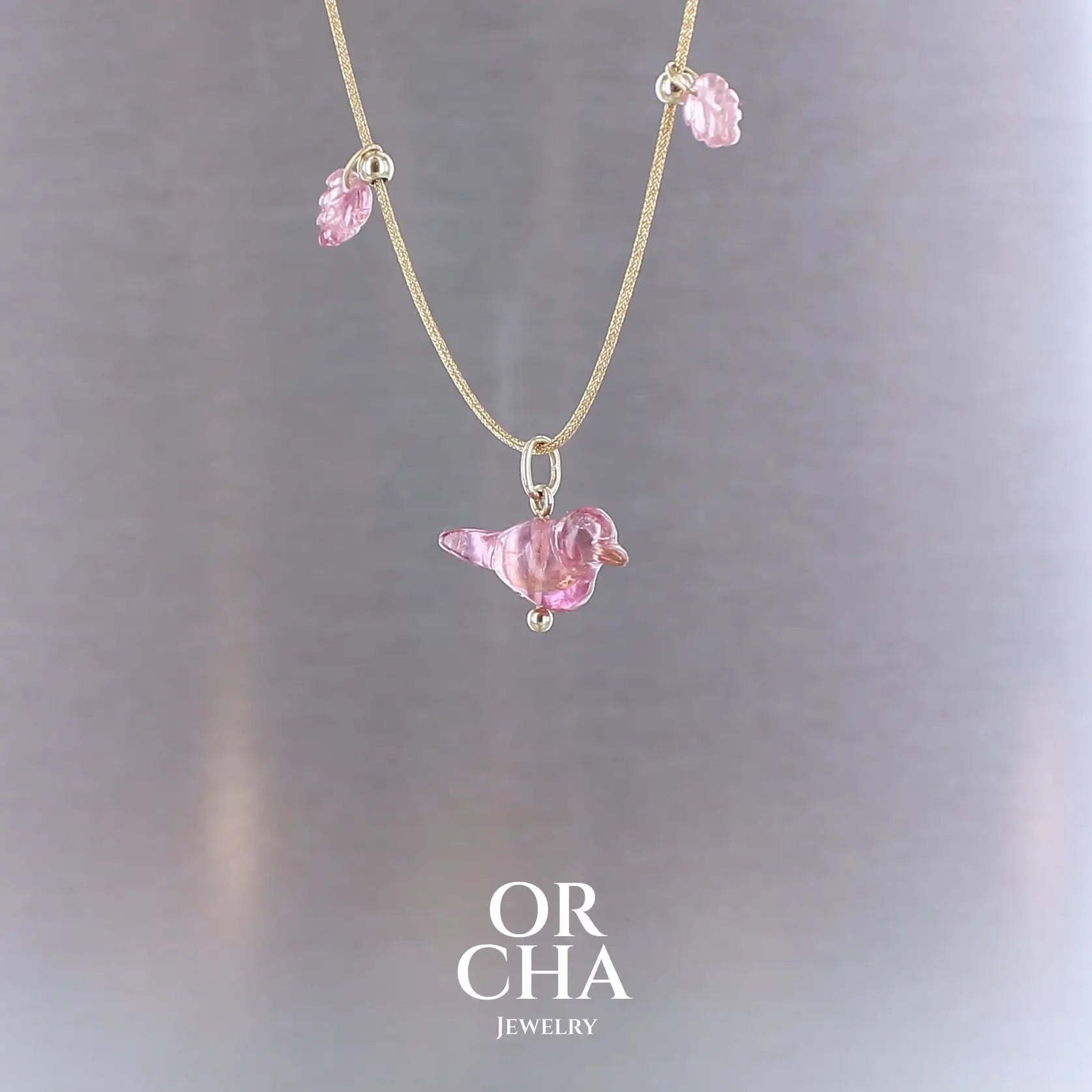 Collier pour femme orné de tourmalines roses sculptées à la main en 3 dimensions en forme d'oiseau et de feuilles, serties en or 18k. Les pendentifs sont montés sur un collier corde doré scintillant, les apprêts utilisé sont en Gold filled ( or laminé ). Longueur ajustable de 40 cm à 45 cm. Bijoux unique, éthique et durable présenté dans un coffret de notre marque, prêt à offrir. Livraison offerte, certificat d'authenticité, service client.