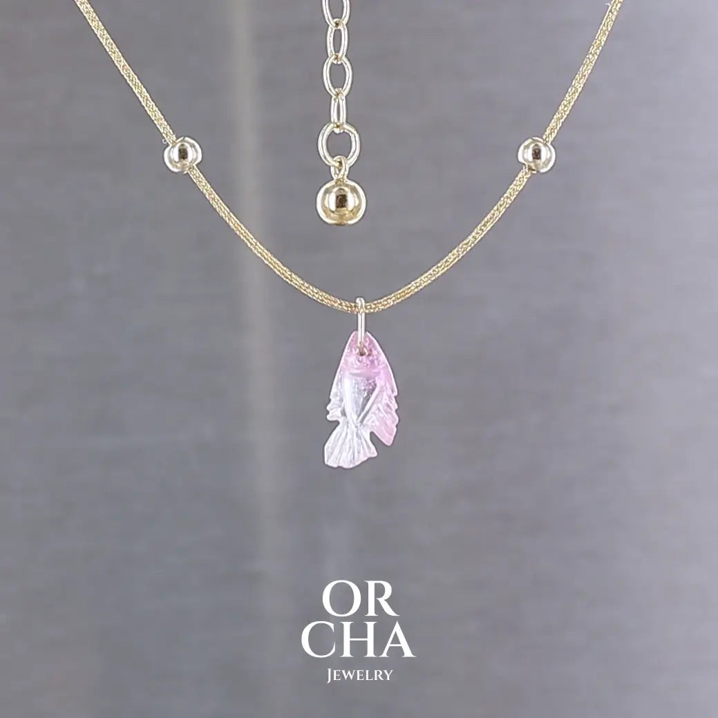 Collier pour femme orné d'une tourmaline rose sculptée à la main en 3 dimensions en forme de poisson sertie en or 18k. Le pendentif est monté sur un collier corde doré scintillant, les apprêts utilisé sont en Gold filled ( or laminé ). Longueur ajustable de 40 cm à 45 cm. Bijoux unique, éthique et durable présenté dans un coffret de notre marque, prêt à offrir. Livraison offerte, certificat d'authenticité, service client.
