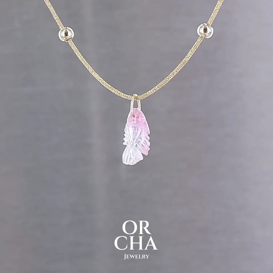 Collier pour femme orné d'une tourmaline rose sculptée à la main en 3 dimensions en forme de poisson sertie en or 18k. Le pendentif est monté sur un collier corde doré scintillant, les apprêts utilisé sont en Gold filled ( or laminé ). Longueur ajustable de 40 cm à 45 cm. Bijoux unique, éthique et durable présenté dans un coffret de notre marque, prêt à offrir. Livraison offerte, certificat d'authenticité, service client.