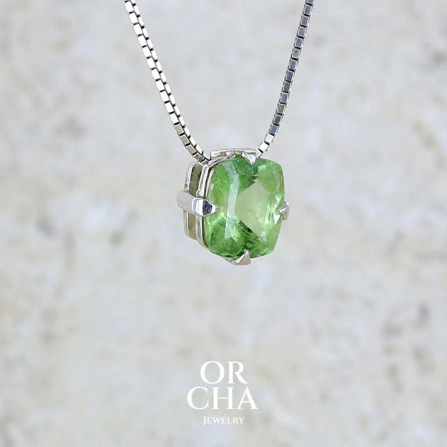 détail collier solitaire pour femme en argent massif sertie d'un Péridot de couleur vert pastel anisé. Pierre facettée de forme carrée, qualité transparente présentant des inclusions. Pendentif monté sur une chaine en argent sterling de type maille miroir de 1,3 mm d'épaisseur et de 40cm de longueur. Bijoux unique réalisé par Orchajewelry