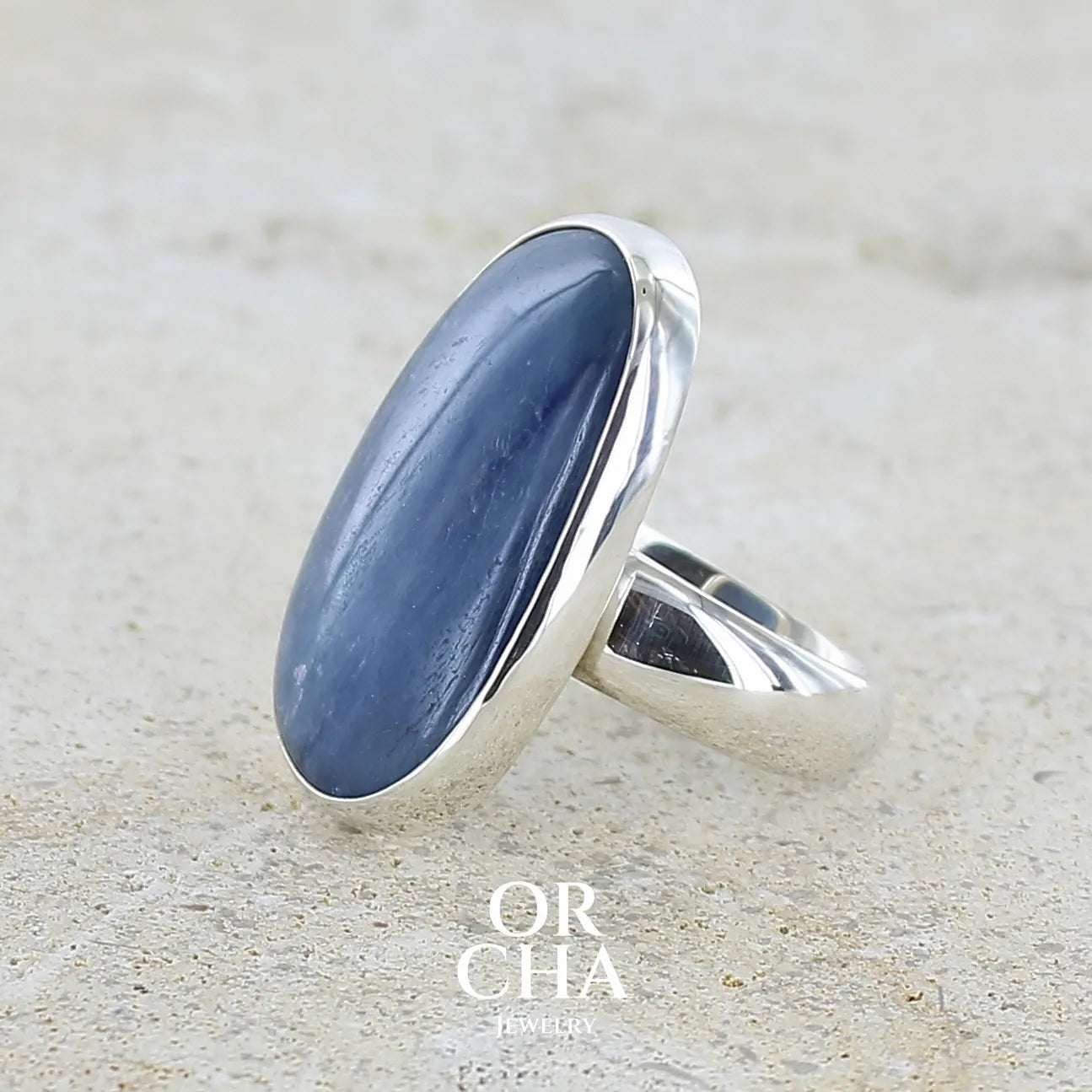 détail du sertissage d'une bague pour femme en argent massif sertie d'un cabochon de cyanite de couleur bleu jean nacré. Pierre translucide à inclusions de forme ovale arrondie. Bijou unique réalisée en taille 58,5 par Orchajewelry