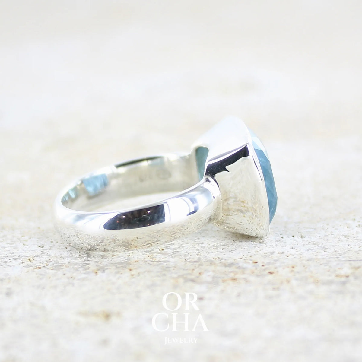 Détail de l'anneau d'une Bague cocktail pour femme en argent massif sertie d'une aigue marine taillée de 10 carats de couleur bleue gris foncé, pierre transparente avec inclusions. Pierre naturelle facettée de forme rectangulaire. Bijoux unique réalisée en taille 60,5 par Orchajewelry