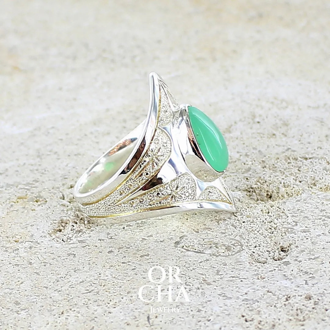 Détail d'une bague étoile pour femme en argent massif sculptées d'étoiles et autres corps célestes sertie d'un cabochon de chrysoprase de couleur verte pastel. Pierre naturelle de qualité translucide taillée goutte. Bague unique réalisée en taille 57 par Orcha jewelry
